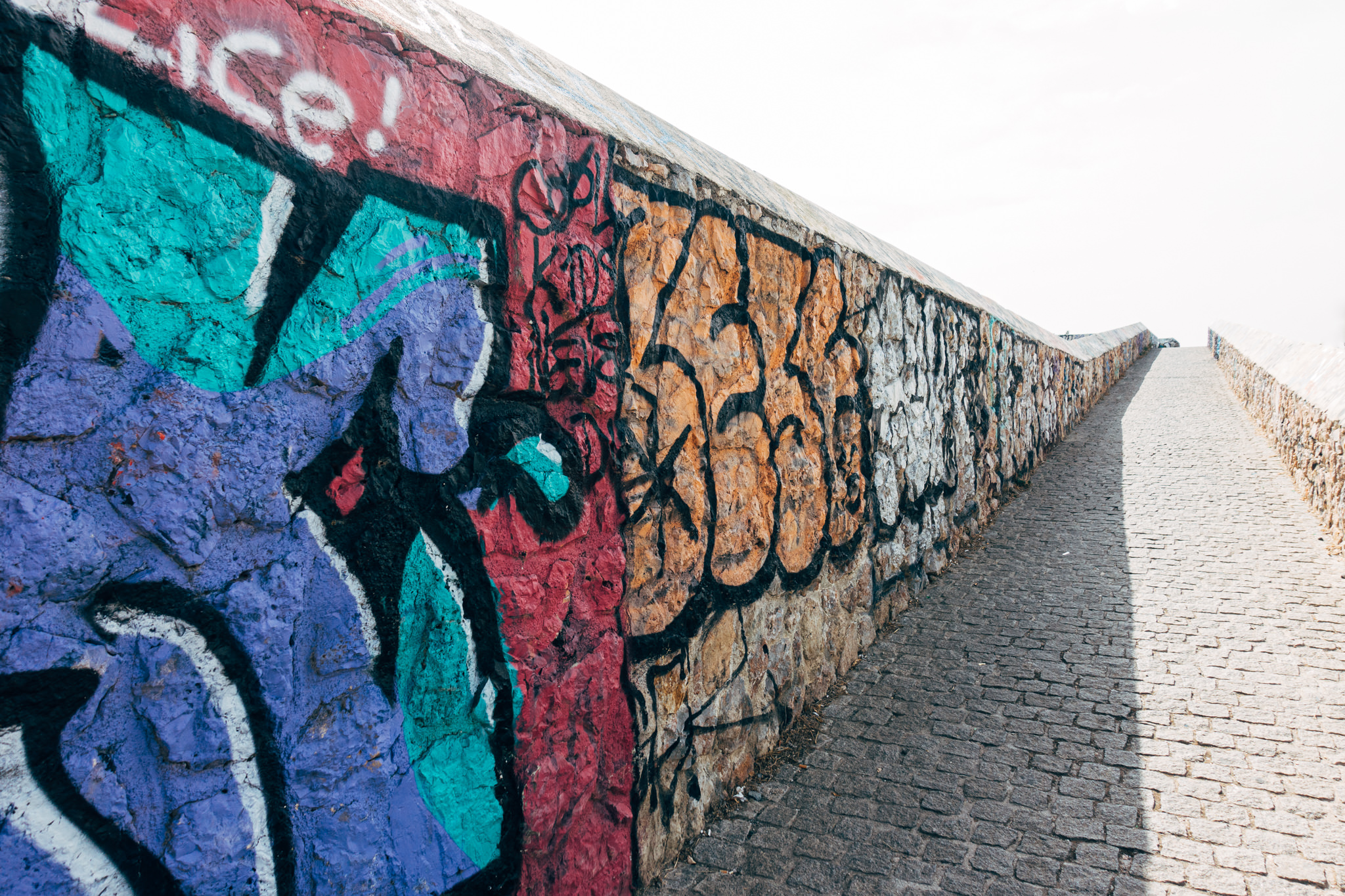 Graffiti on a stone wall next to a cobblestone pathway.