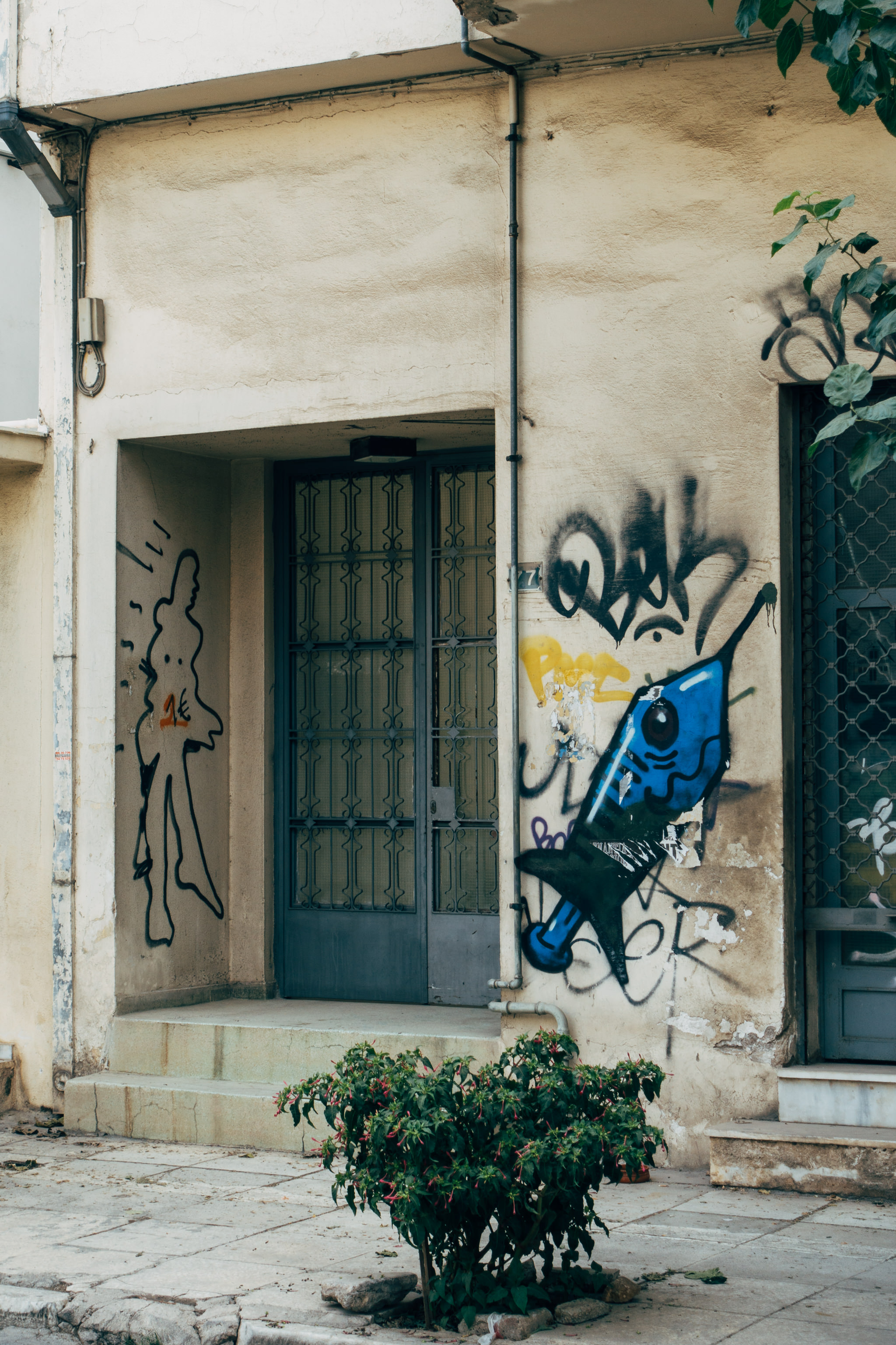 Graffiti on a weathered building in Athens, Greece, featuring a syringe and a stylized figure.