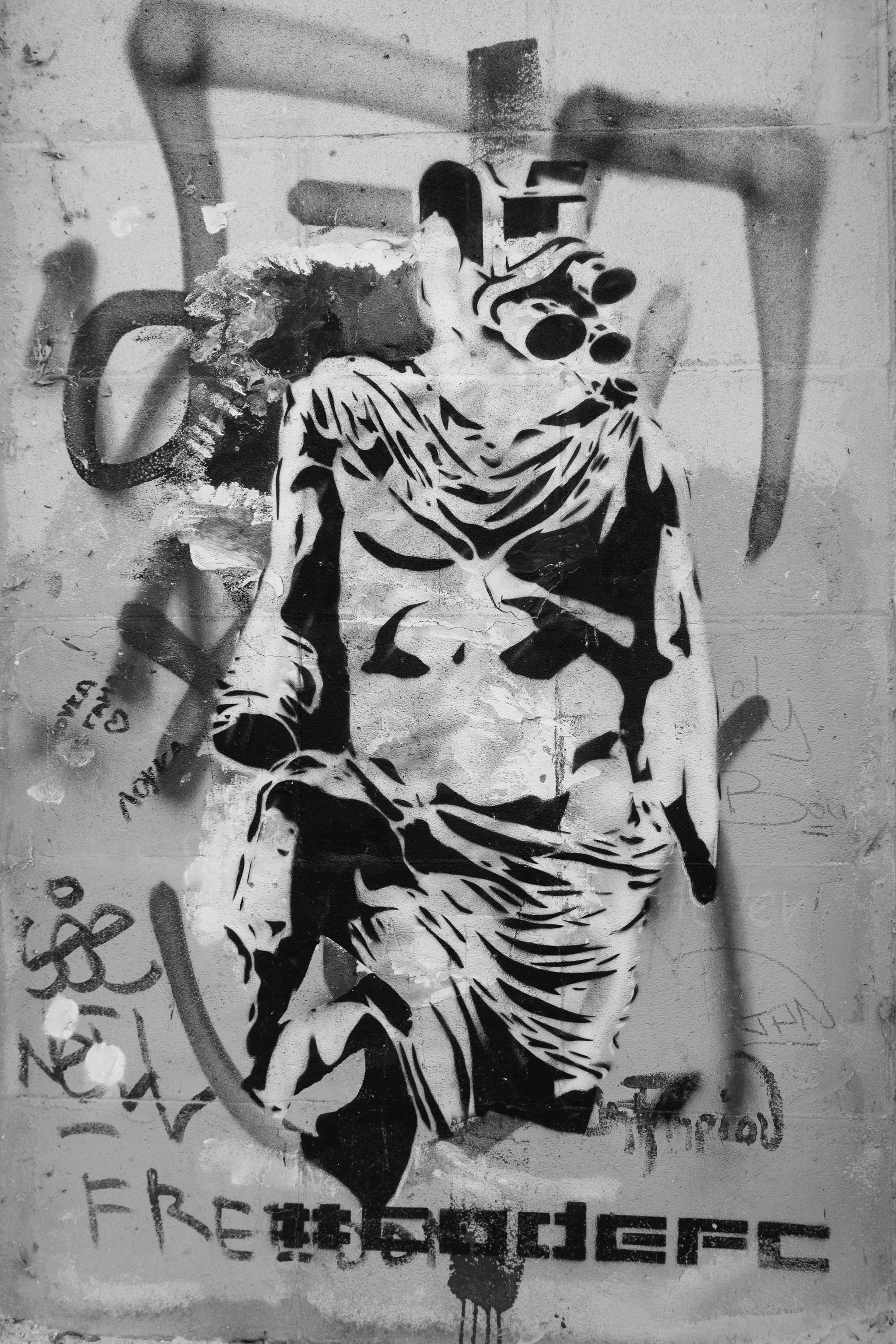 Black and white graffiti stencil of a figure wearing goggles on a textured wall.