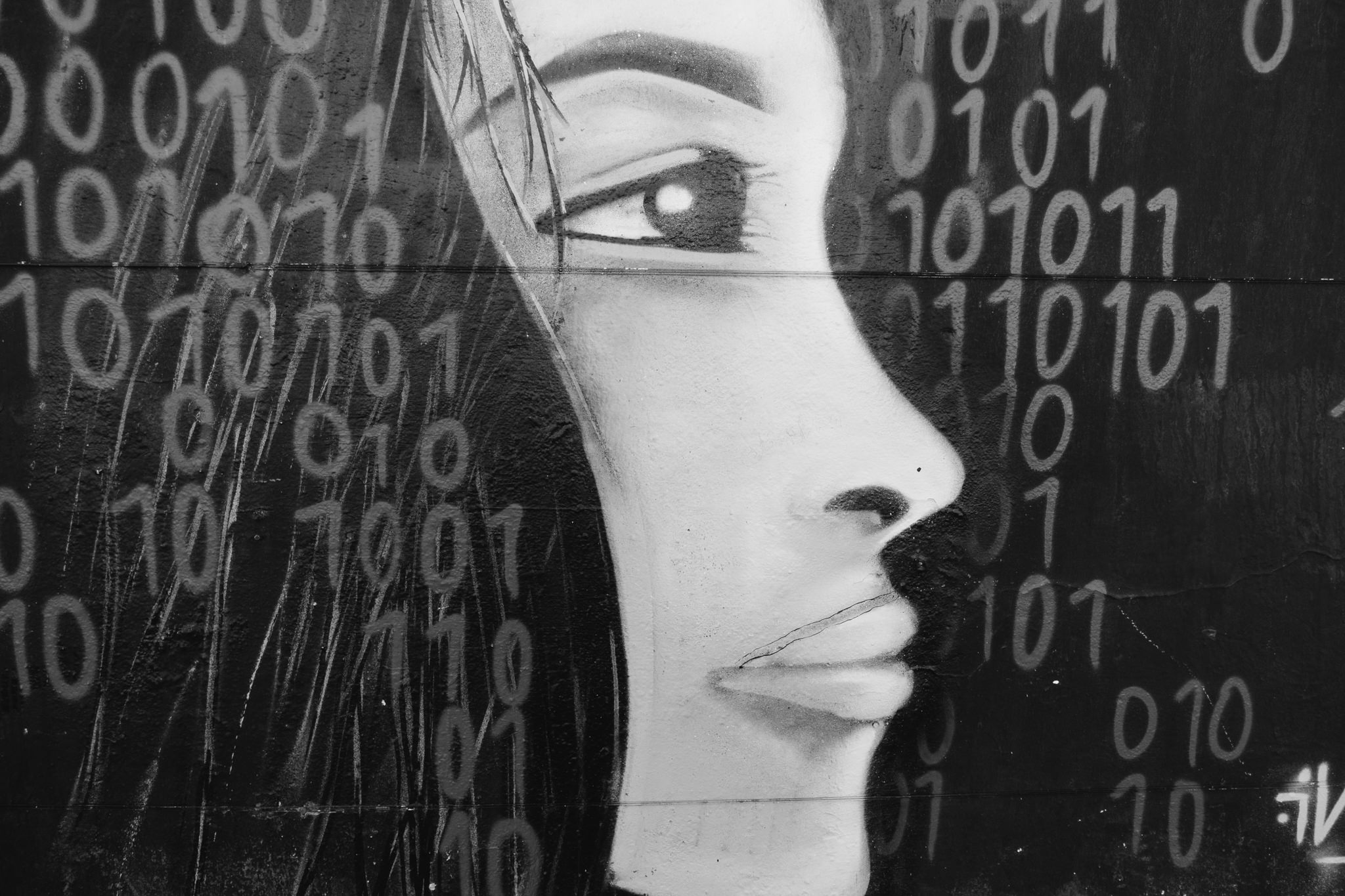 Black and white graffiti of a woman's face overlaid with binary code.
