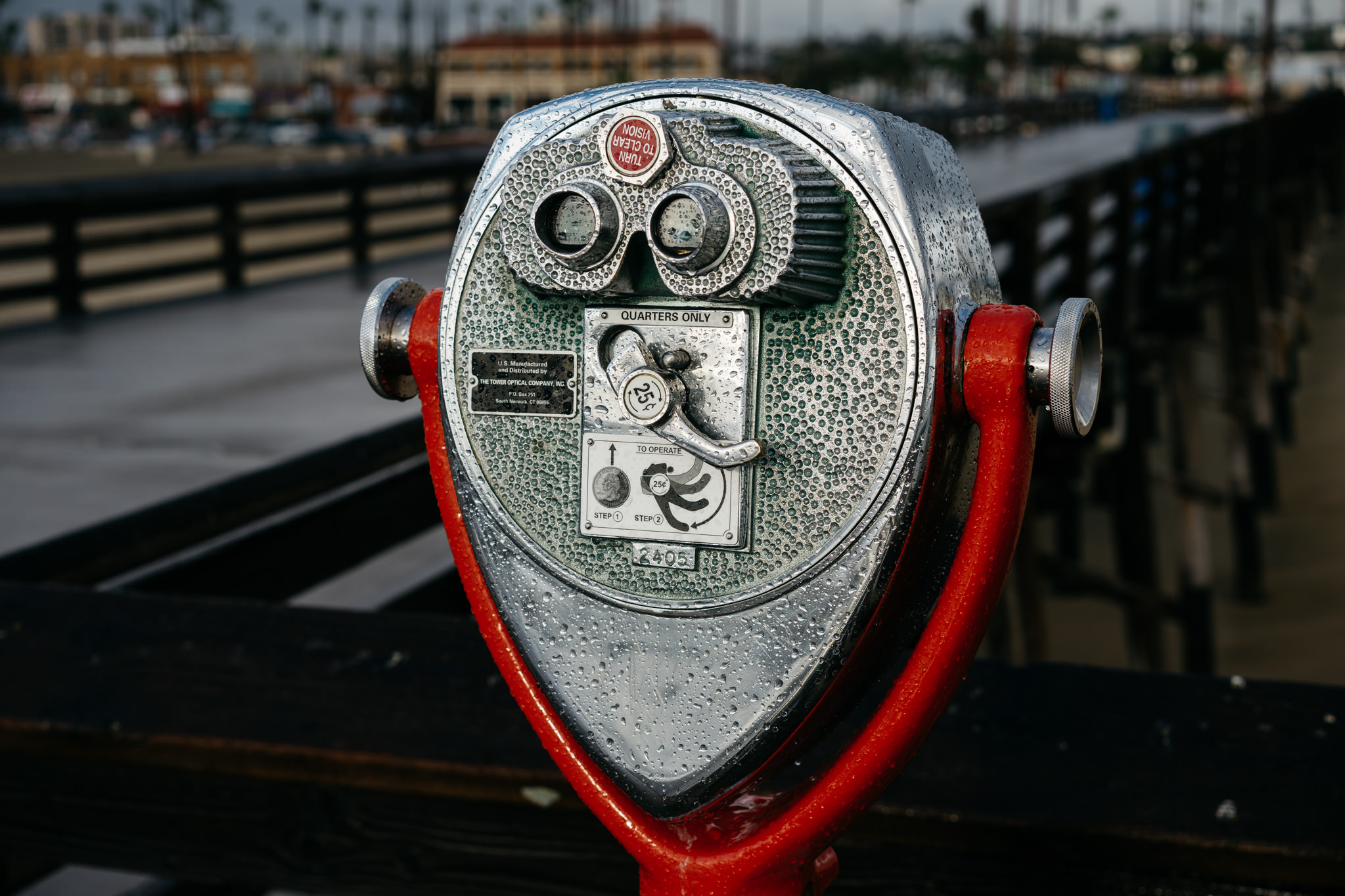 Coin-operated binoculars on a pier, covered in water droplets.