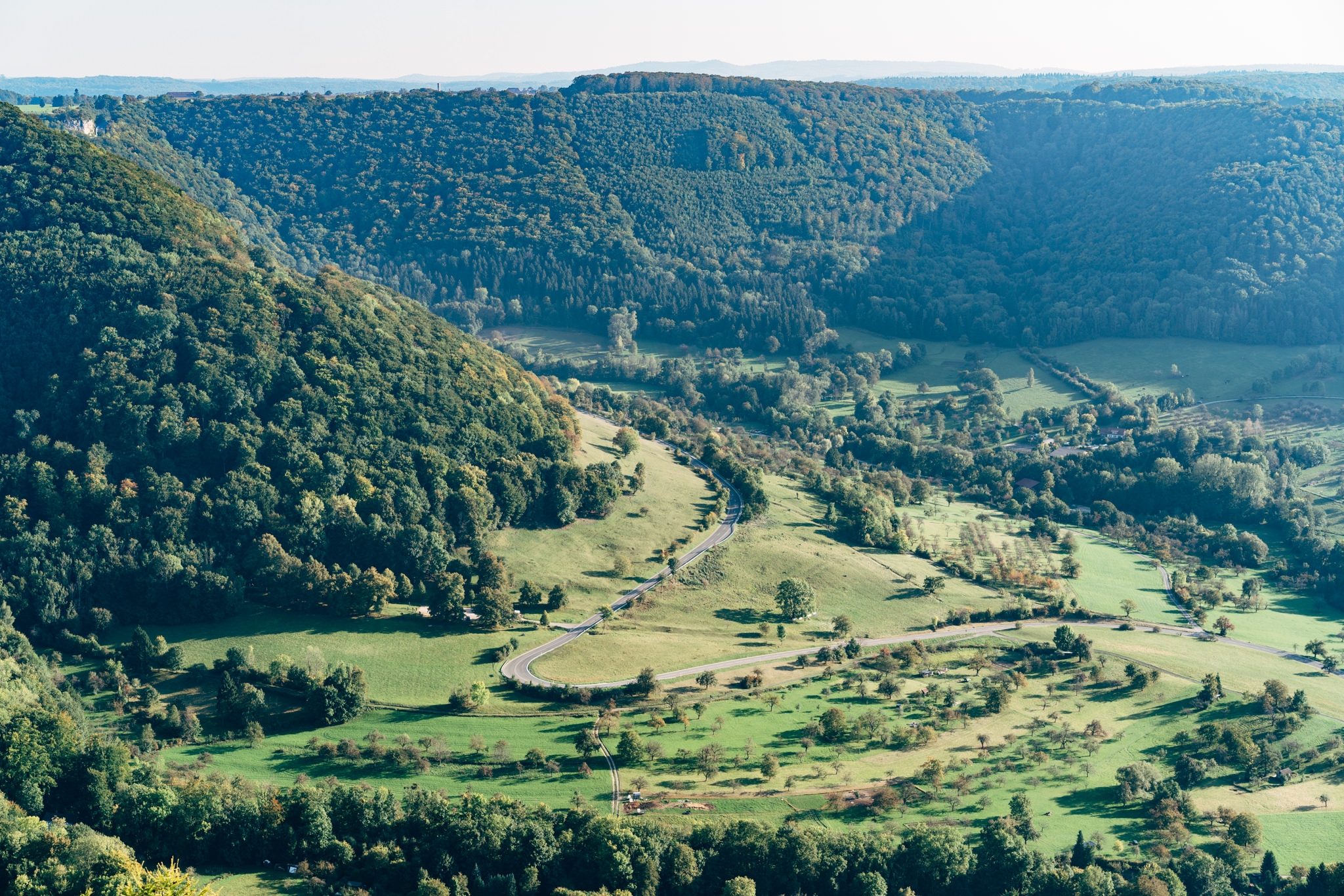 Aerial view of a winding road through a lush green valley and forest.