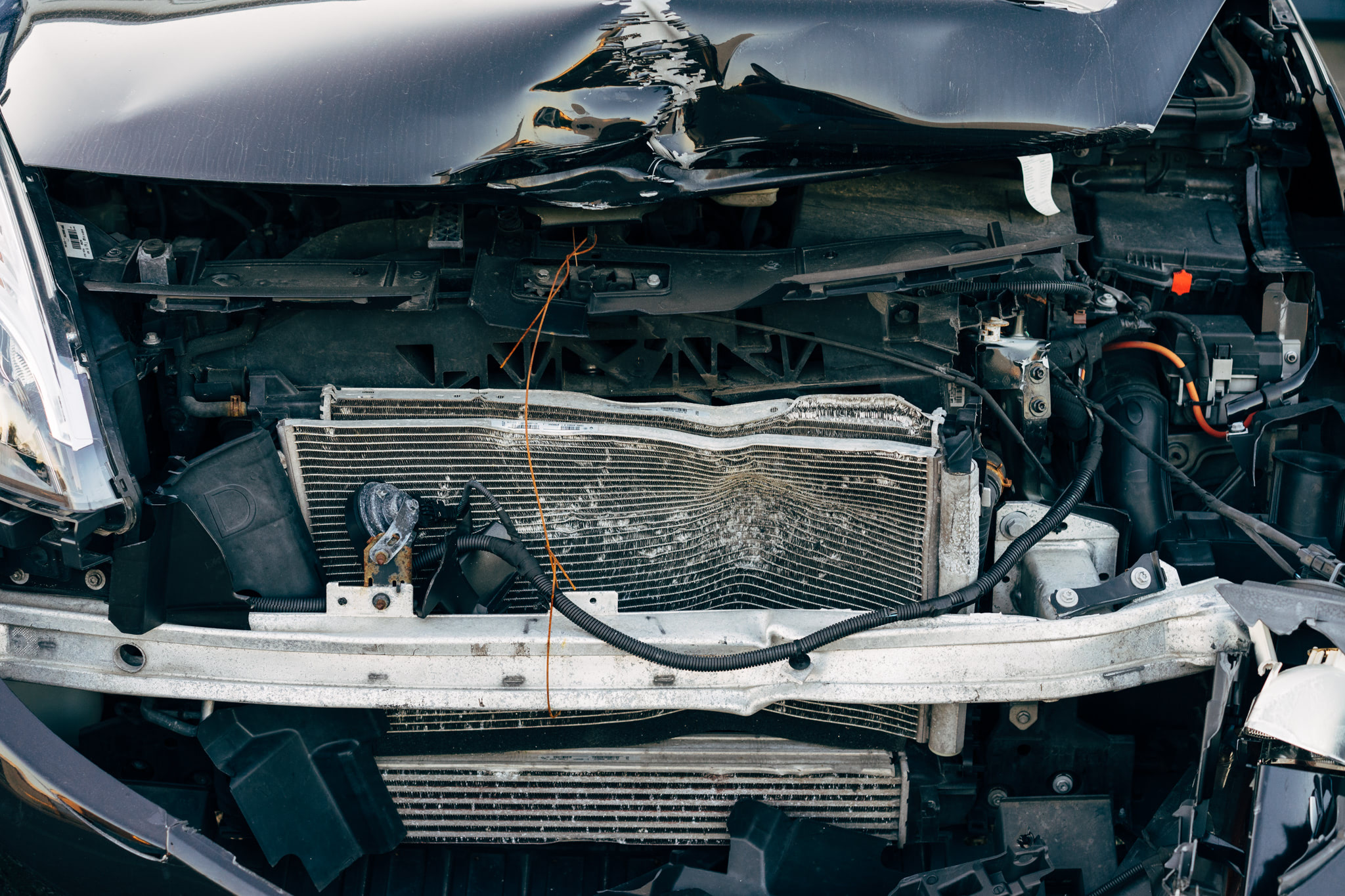 Close-up of a severely damaged car front end, showing exposed engine components and significant structural damage.
