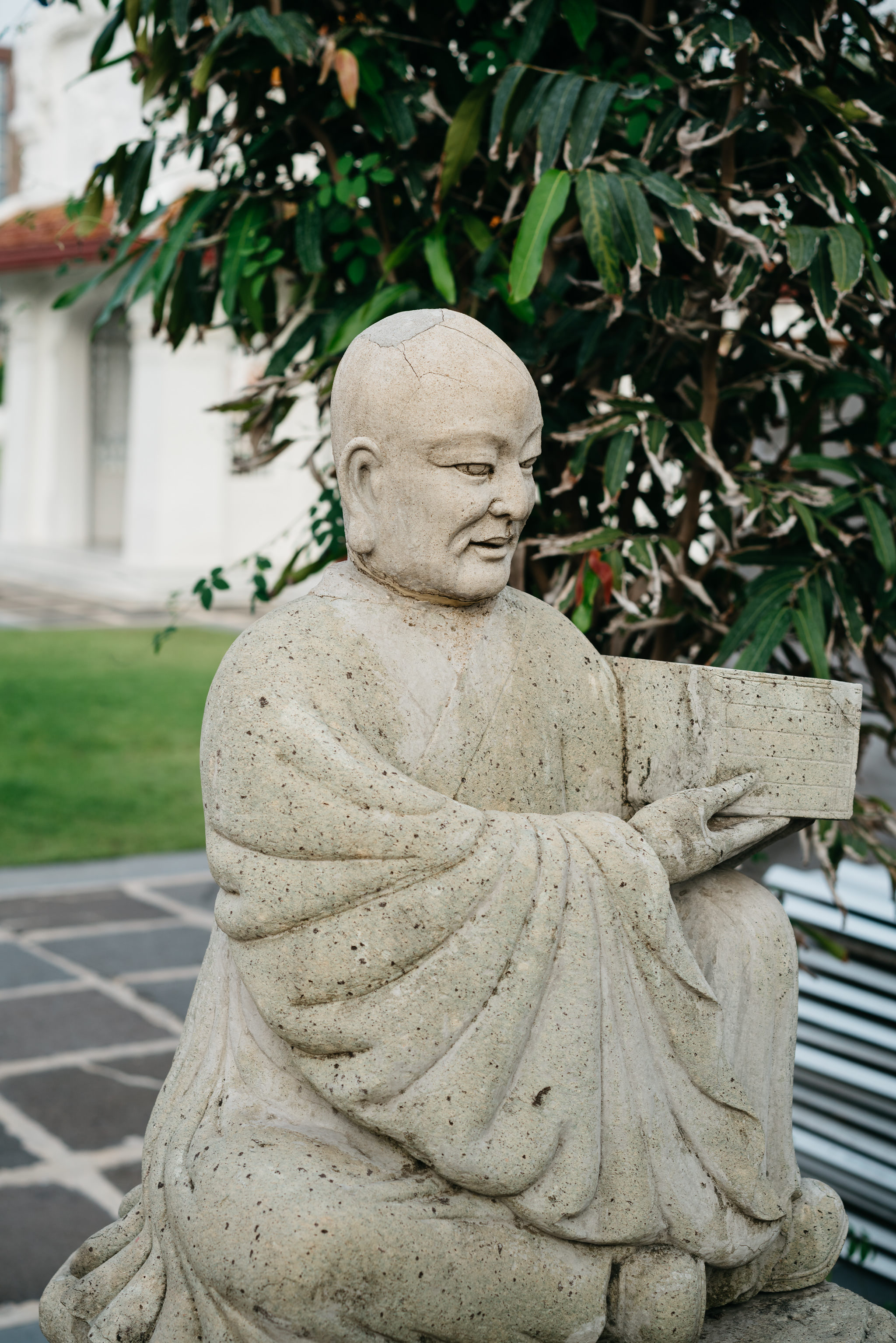Stone statue of a monk seated holding a book at Wat Benchamabophit in Bangkok.