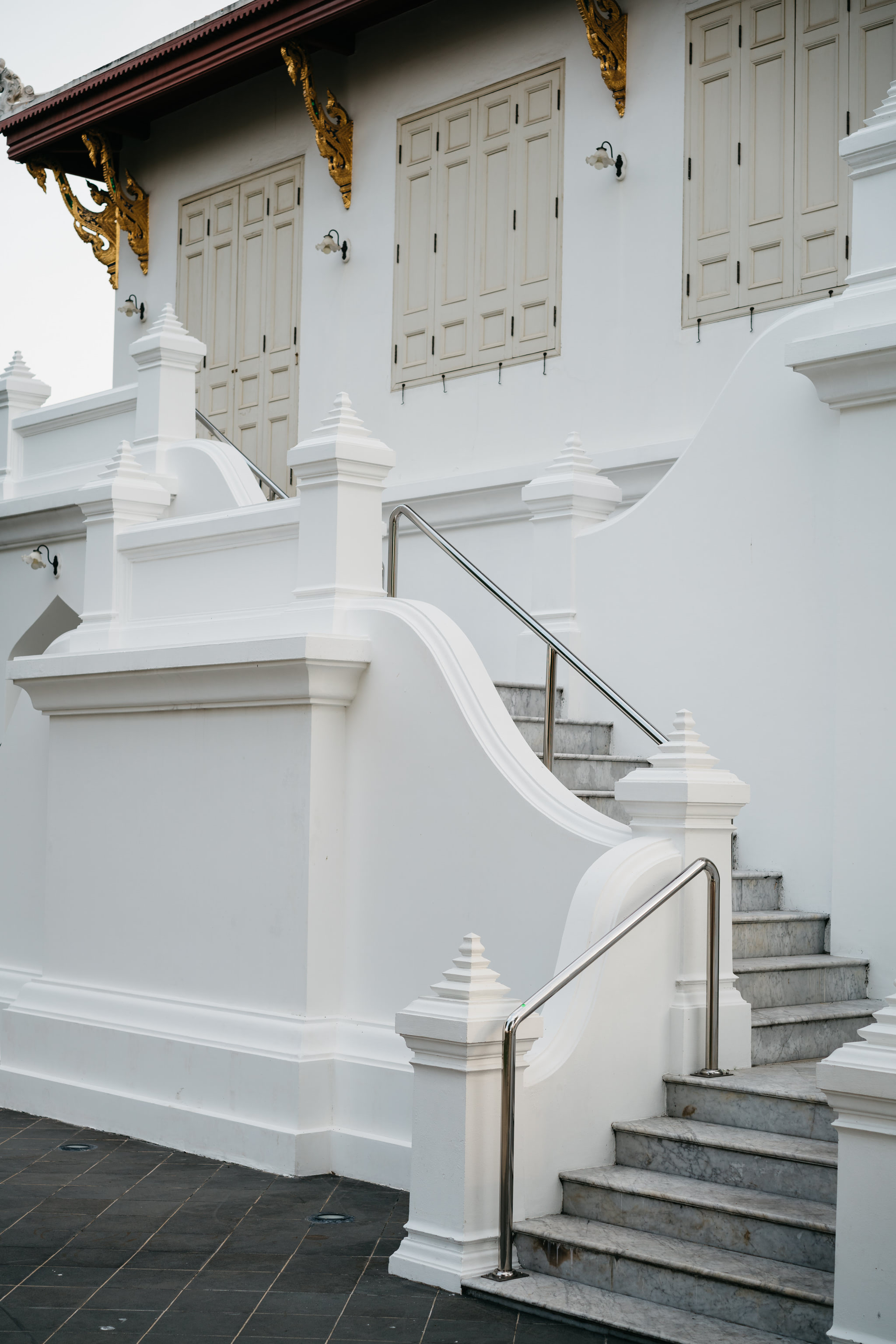 White marble staircase with a metal railing in front of a white building with ornate gold details.