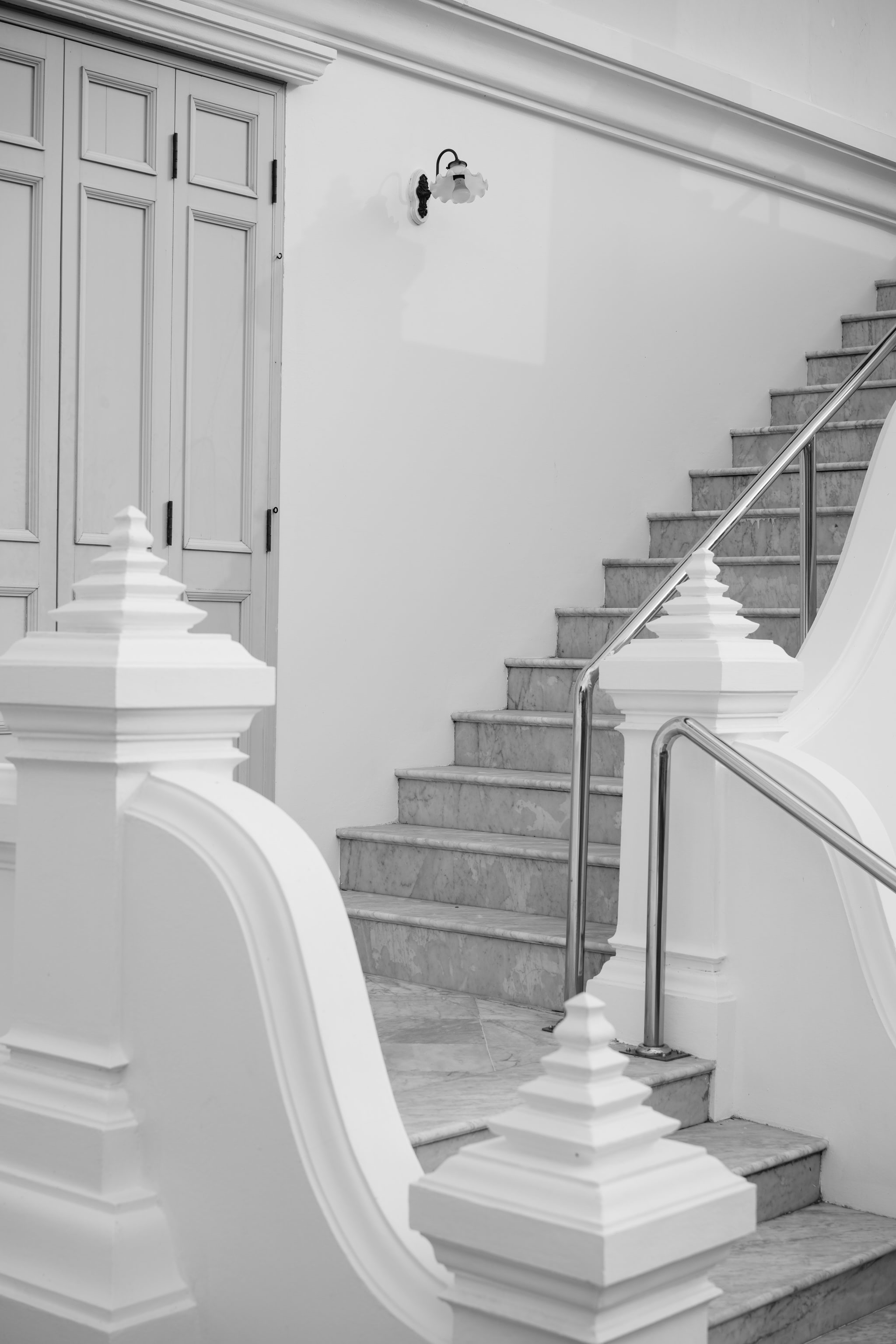 Black and white photo of a marble staircase with a metal railing and white ornate balustrades.