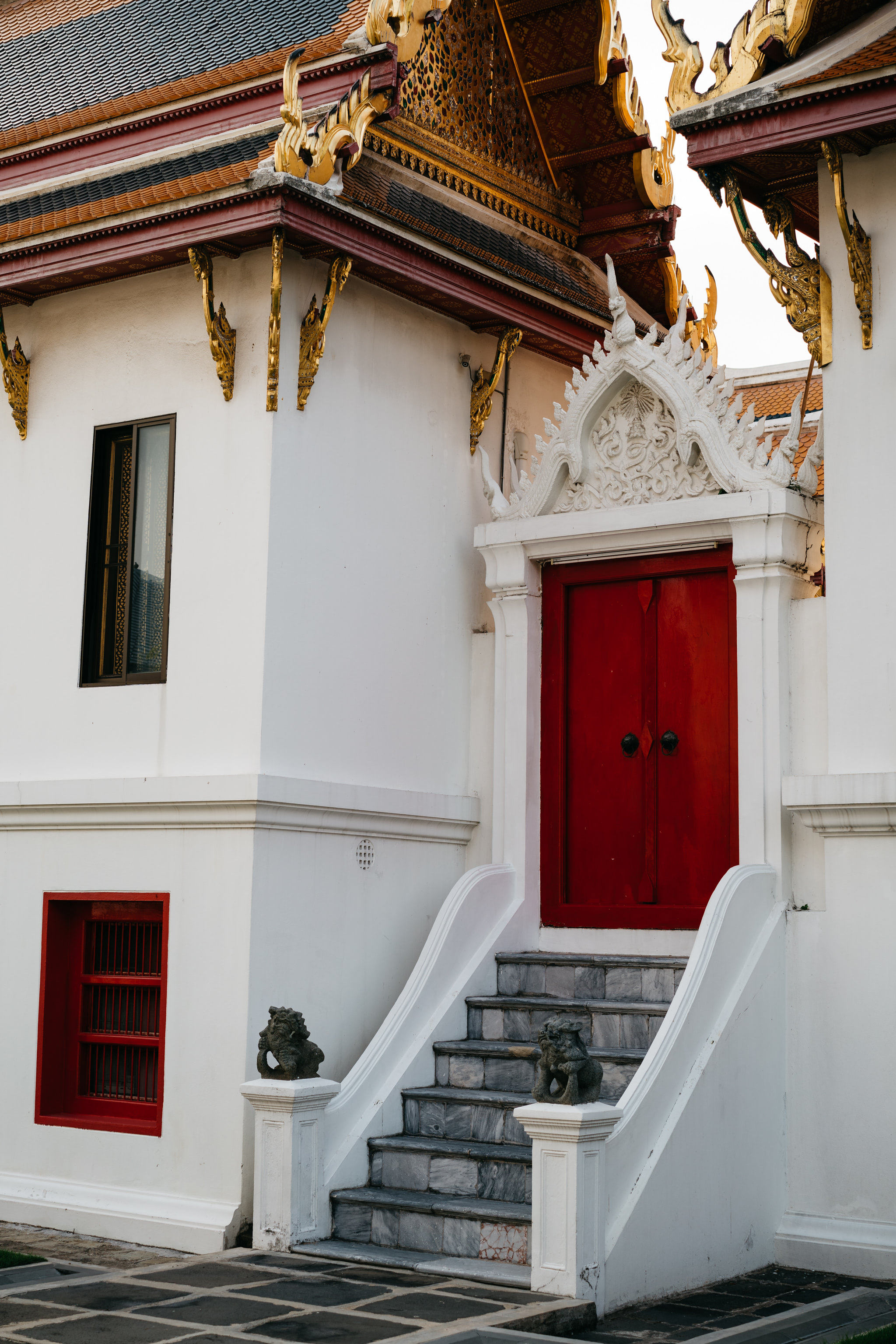 Wat Benchamabophit temple exterior, red door, grey stone steps, white walls, gold detailing.