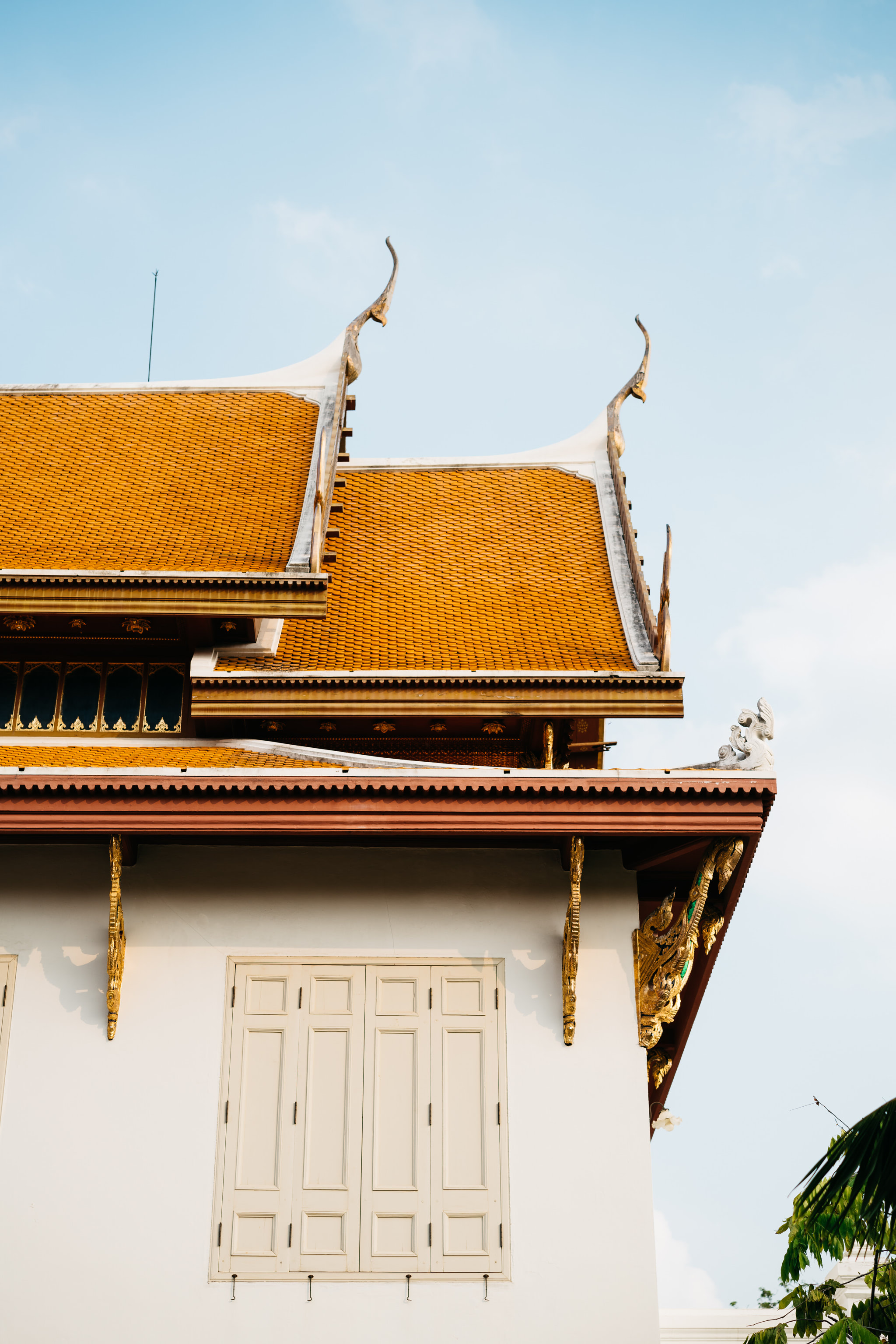 Low-angle view of Wat Benchamabophit's orange tiled roof and white wall with ornate details.