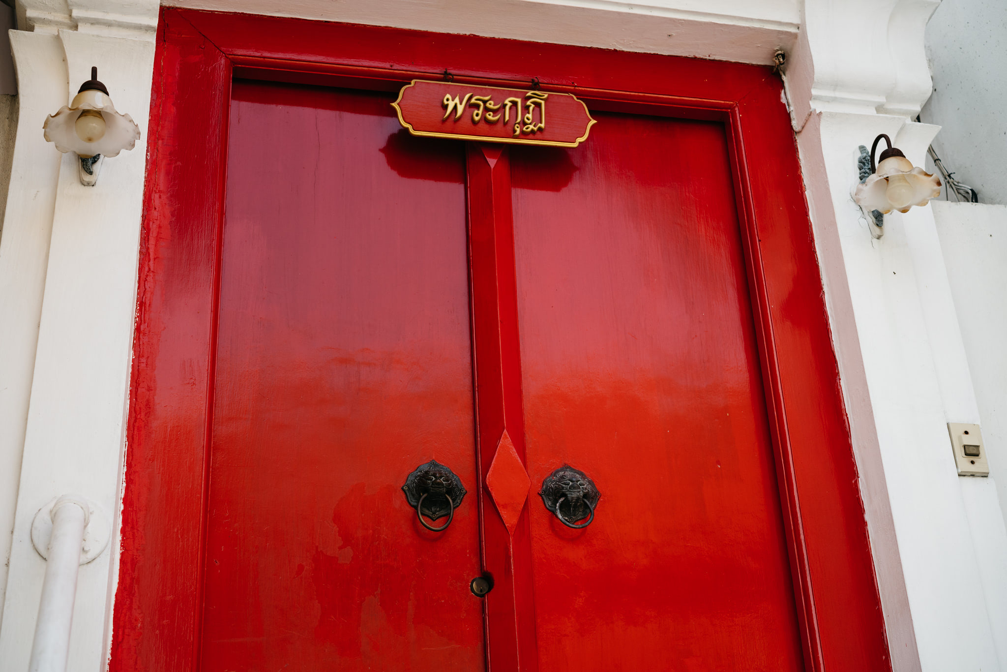 Red double doors with lion-head door knockers and a Thai-language sign.