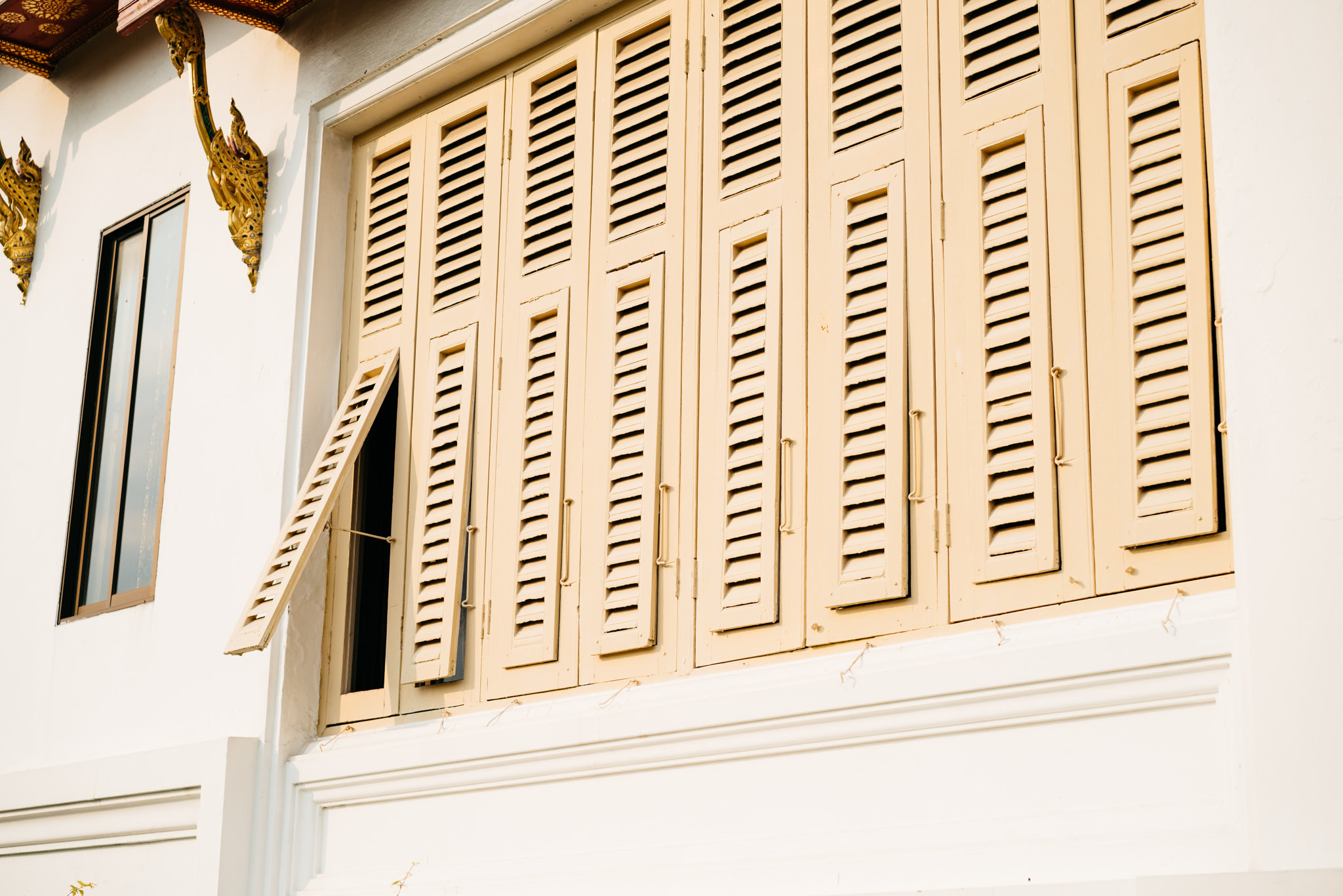 Pale yellow louvered window shutters, one ajar, on a white building.