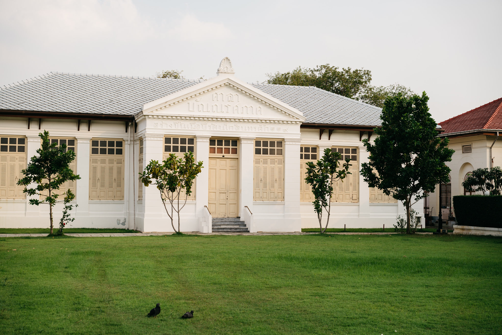 White building with light beige doors and windows, set on a grassy lawn.