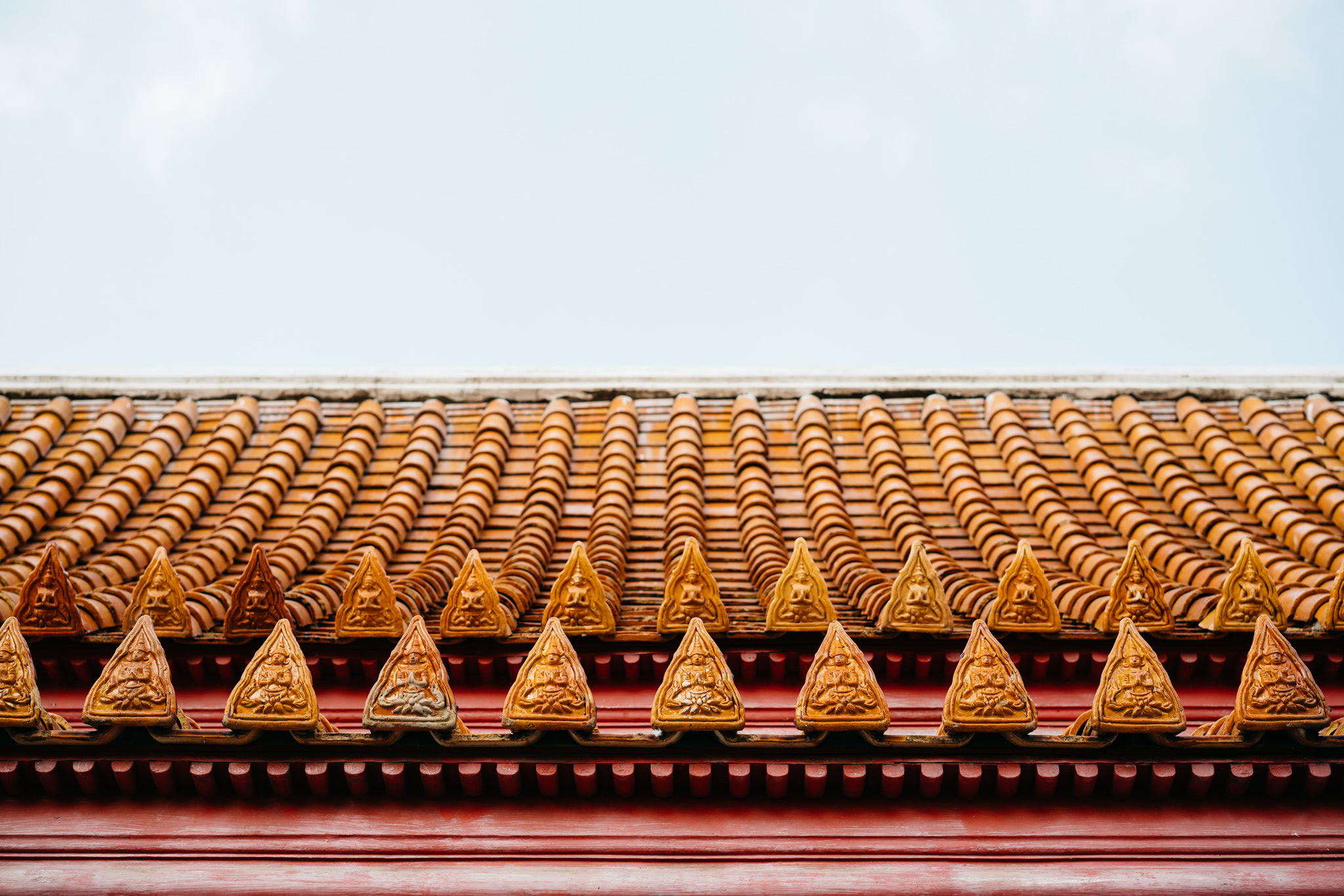 Orange tiled roof with decorative triangular ornaments depicting Buddha figures.
