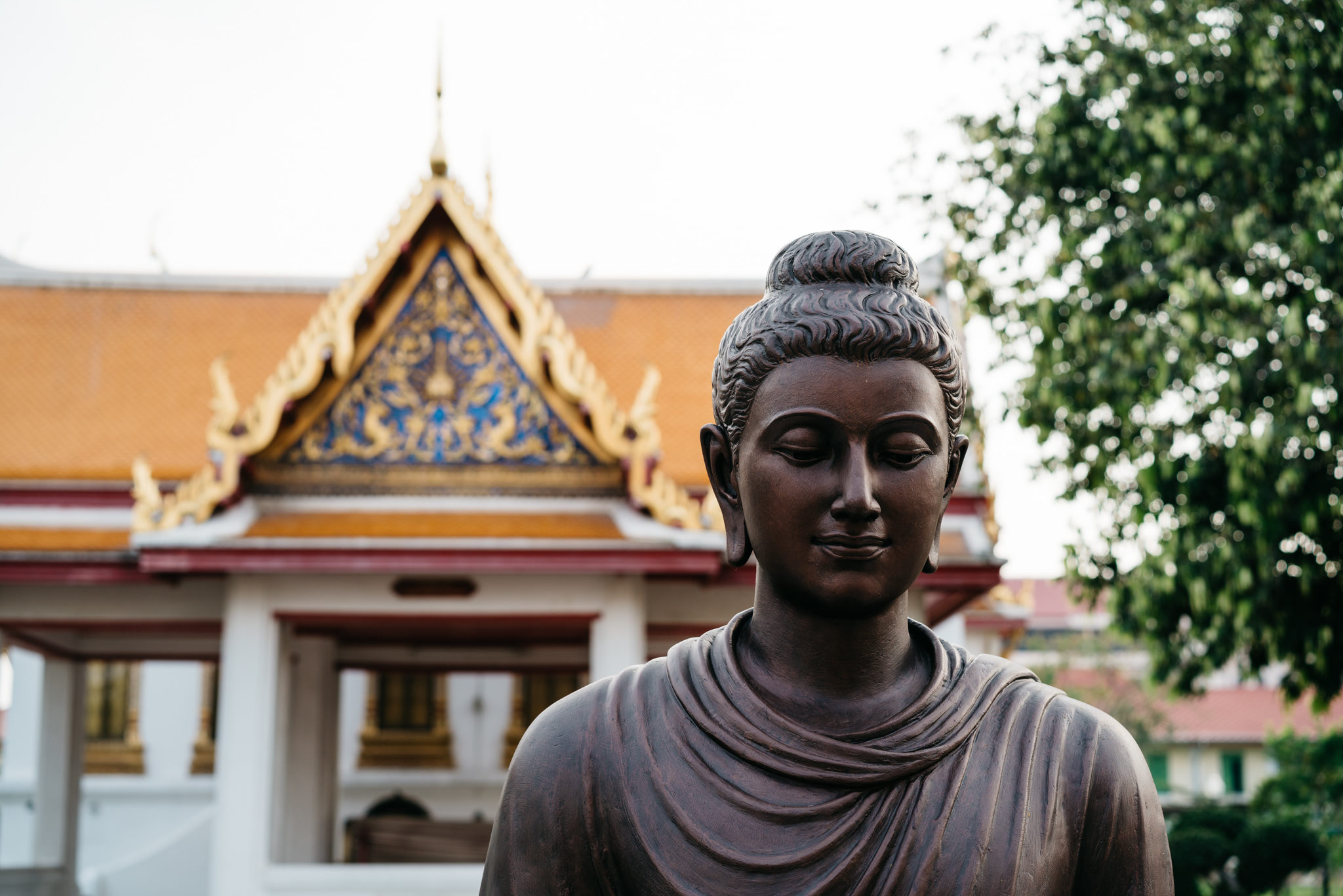 Close-up of a dark bronze Buddha statue in front of a blurred temple.