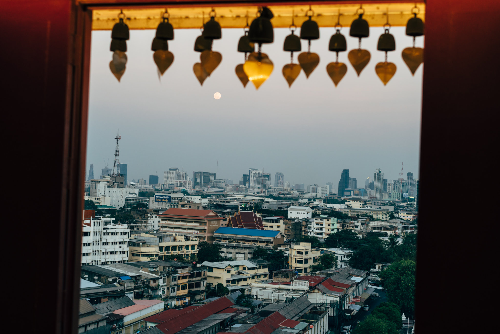 Bangkok cityscape viewed through a window frame adorned with ornate bells.