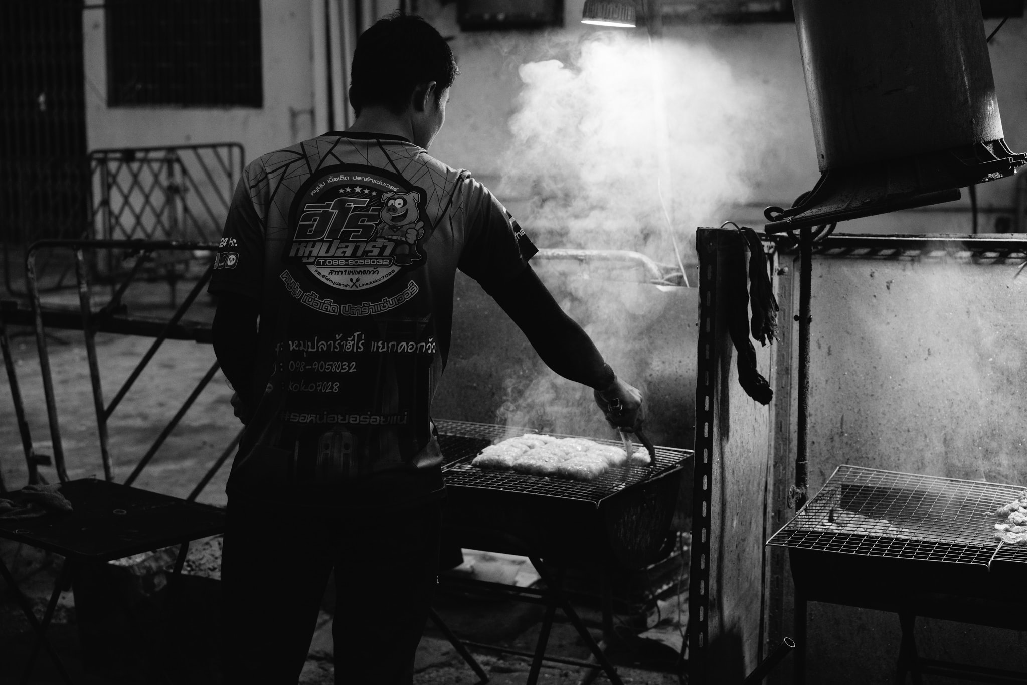 Black and white photo of a person grilling food at night in Bangkok.