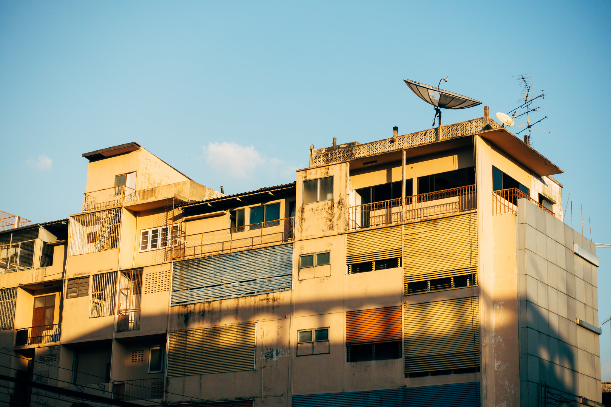 A tan multi-story building in Bangkok at sunset with satellite dishes on the roof.