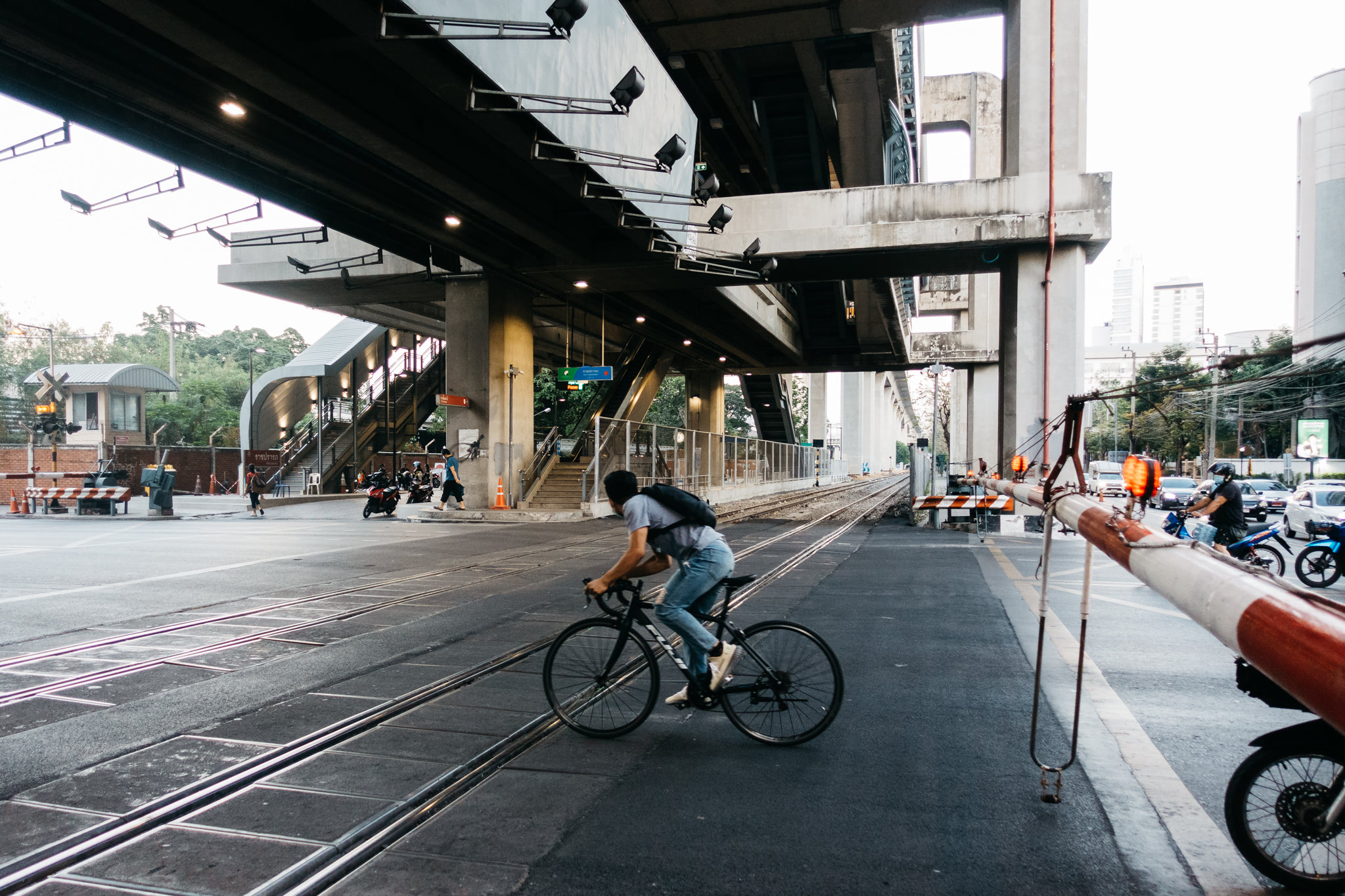 Man cycling across train tracks under Bangkok train station.
