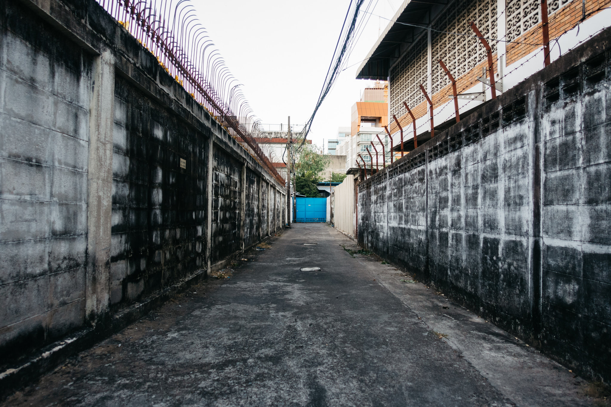 Dark alleyway between weathered concrete walls topped with barbed wire.