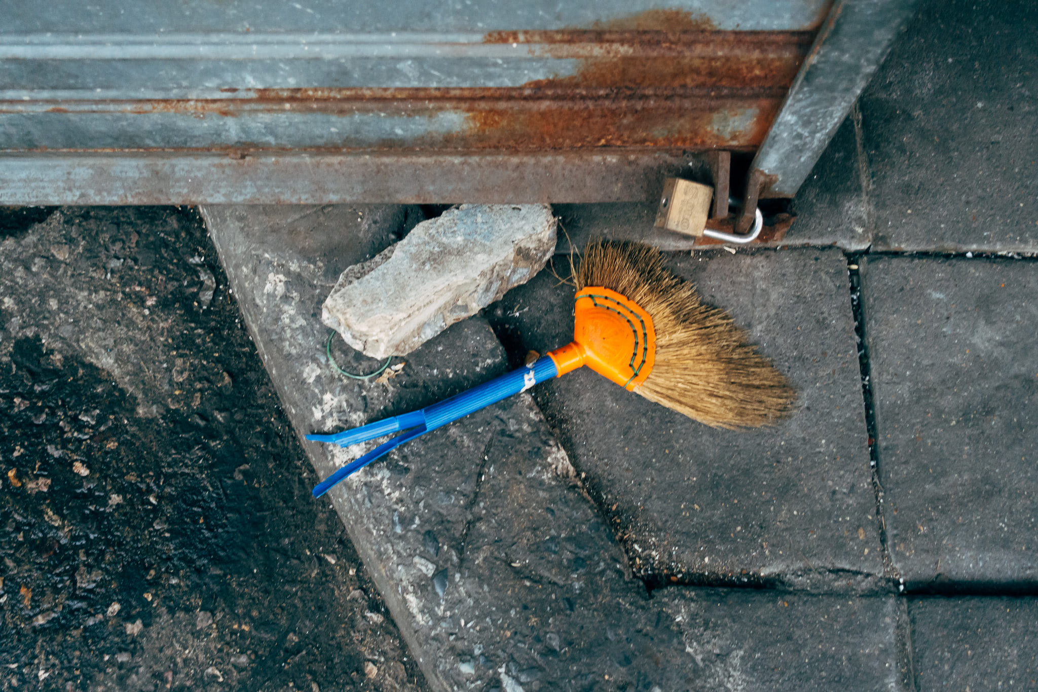 Broom and padlock by rusty metal gate.