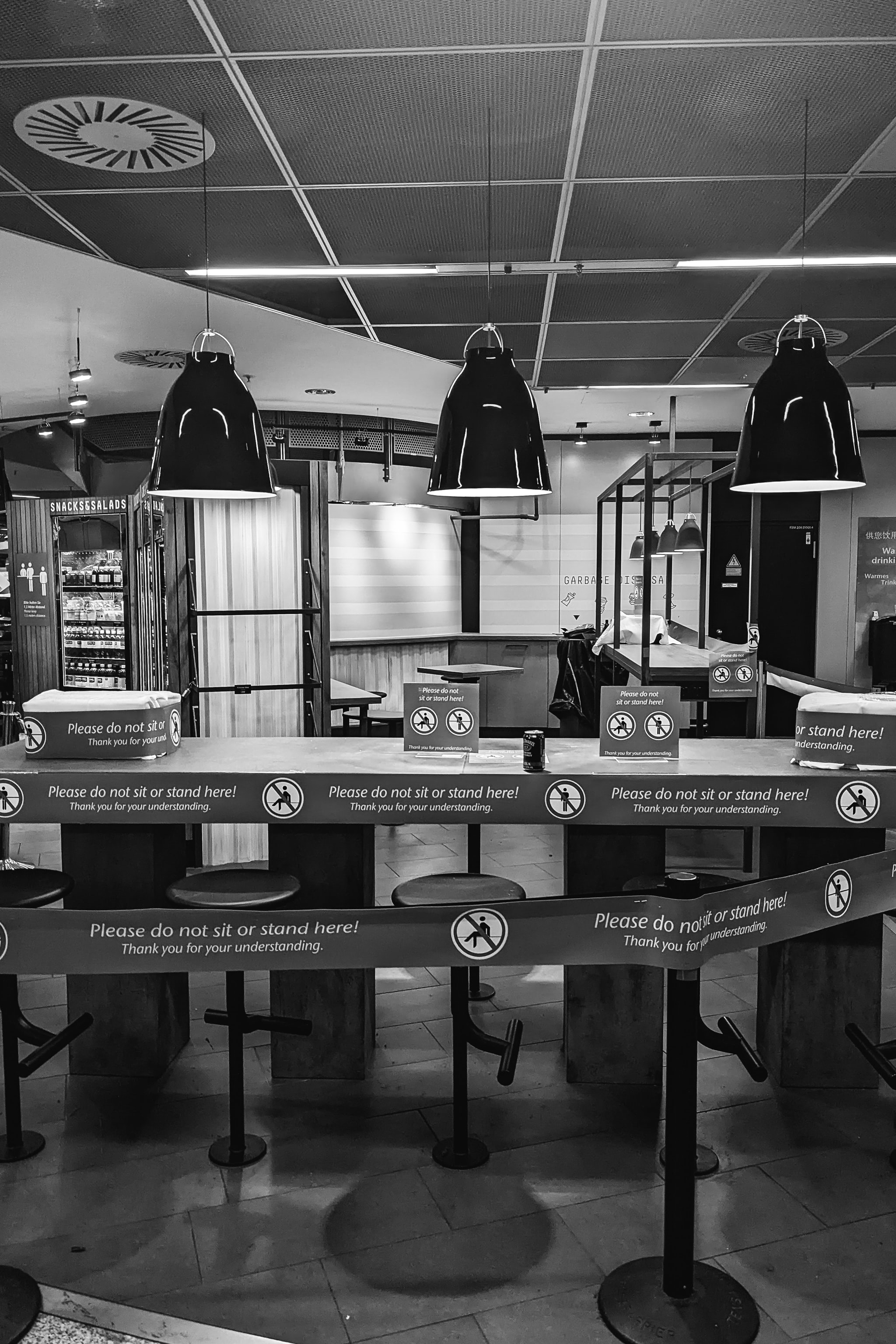 Airport seating area with blocked-off seating and signs indicating 'Please do not sit or stand here!' due to COVID-19 restrictions.