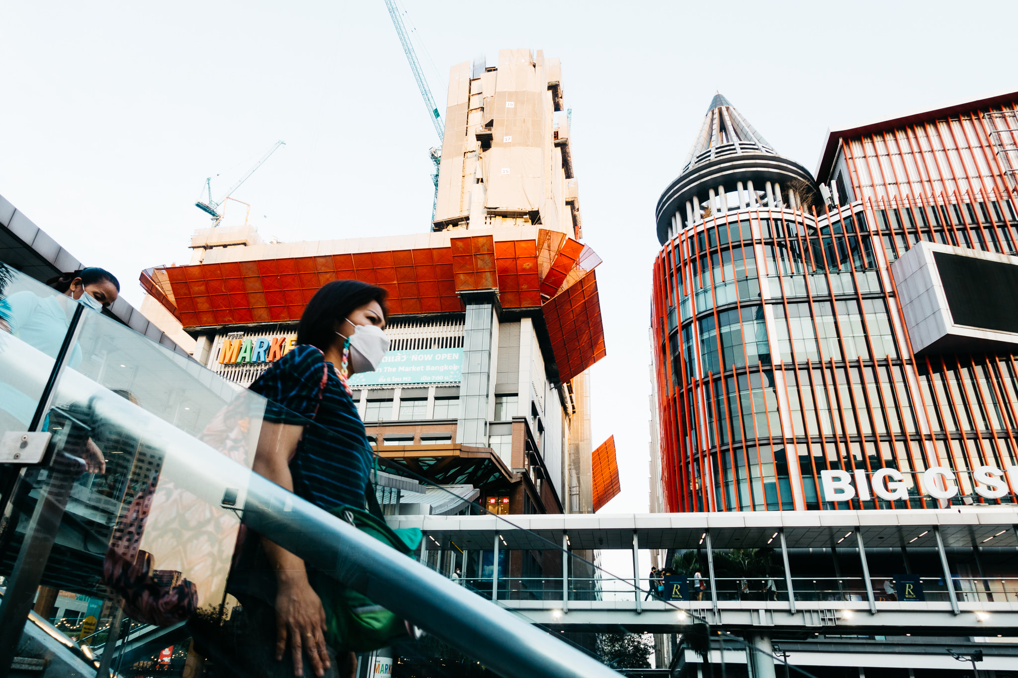 Woman wearing a face mask descends an escalator in front of modern buildings.