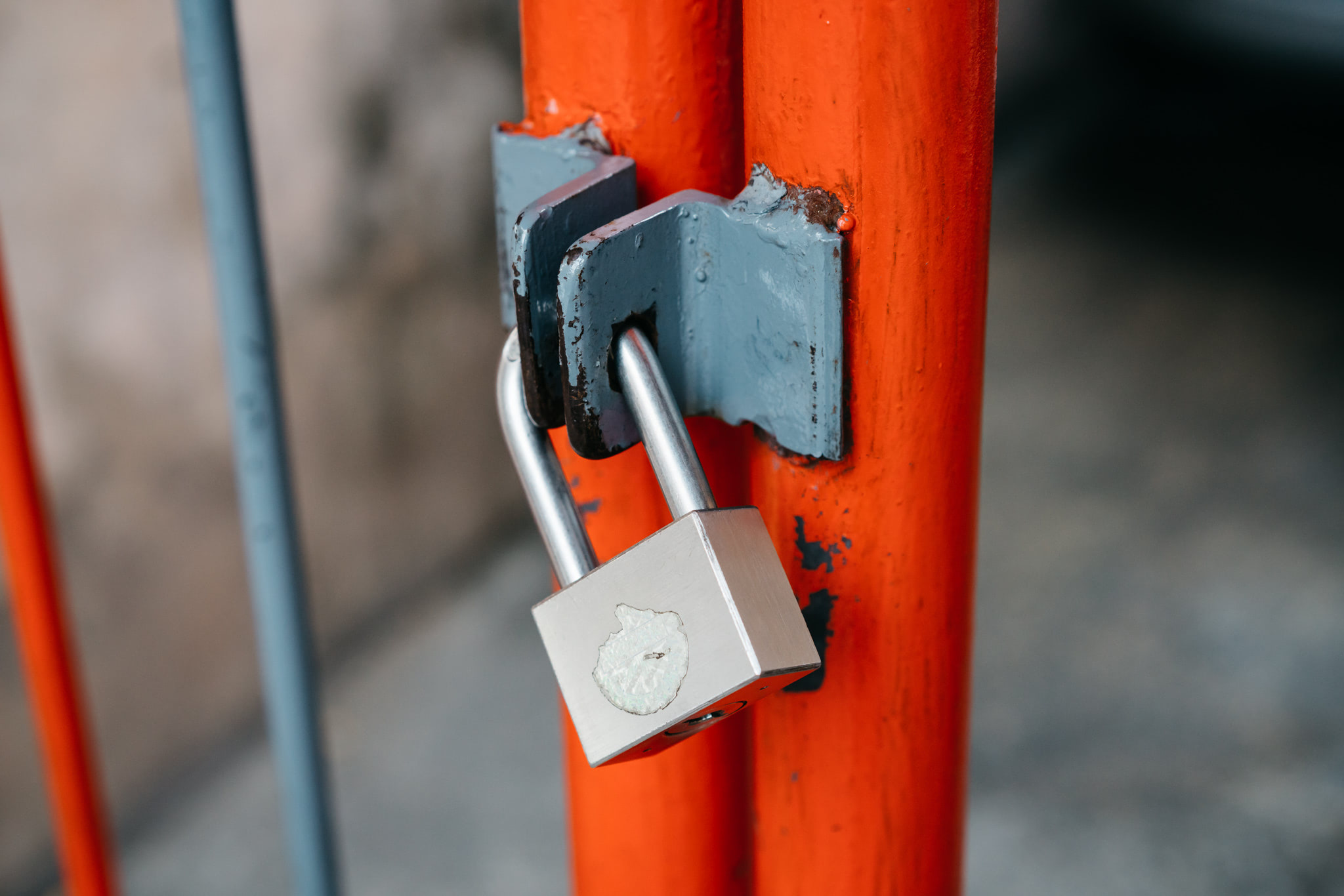 Silver padlock on an orange metal gate.