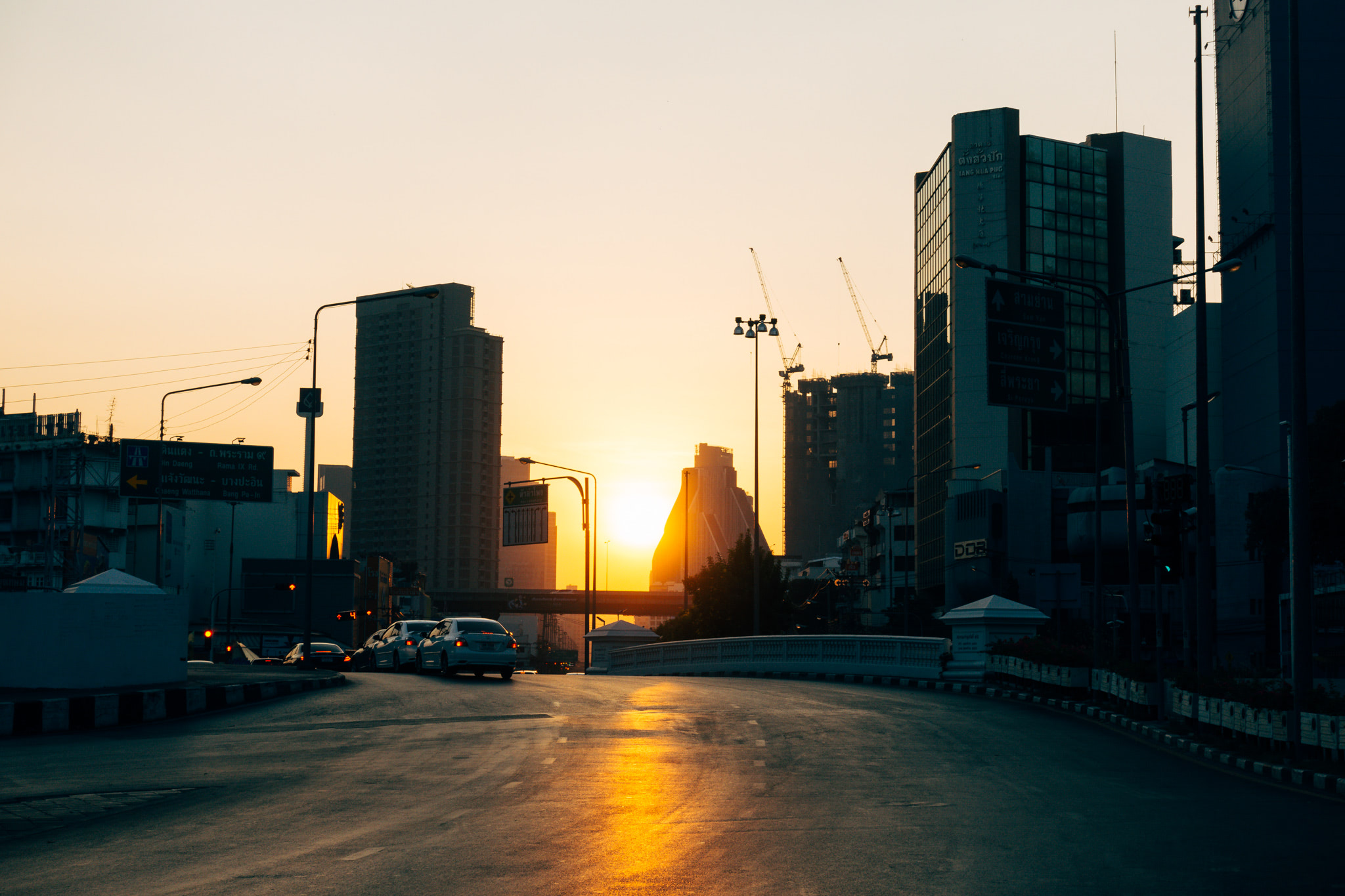 Sunrise over Bangkok street scene with cars and buildings.