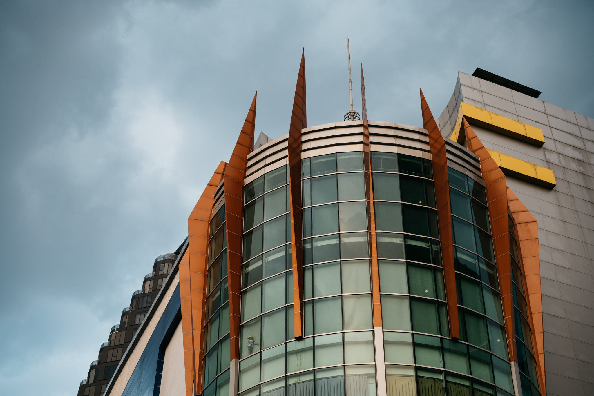 Modern highrise building with orange accents against a cloudy sky.