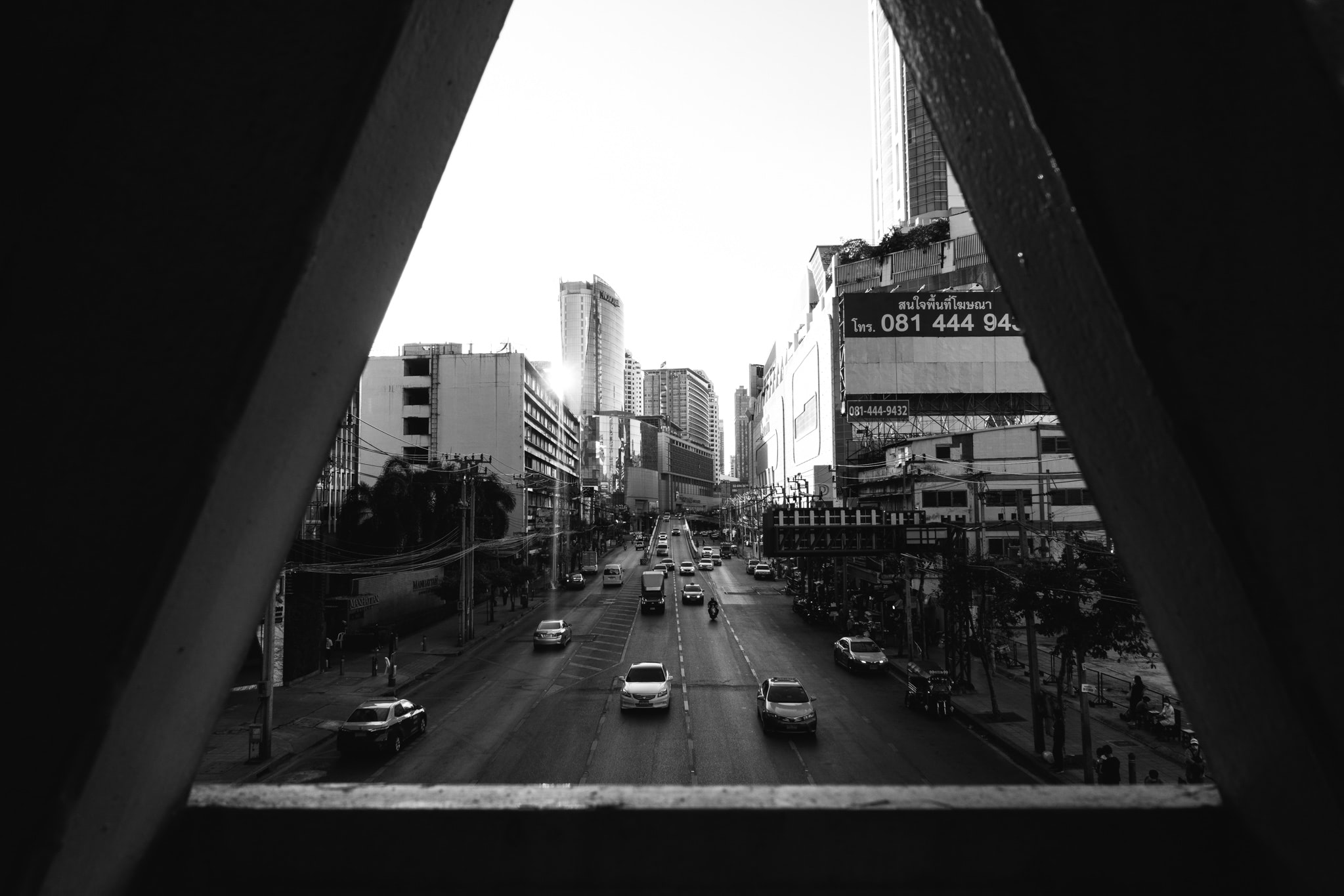 Black and white photo of a Bangkok street scene viewed through a triangular frame, showing traffic and buildings.