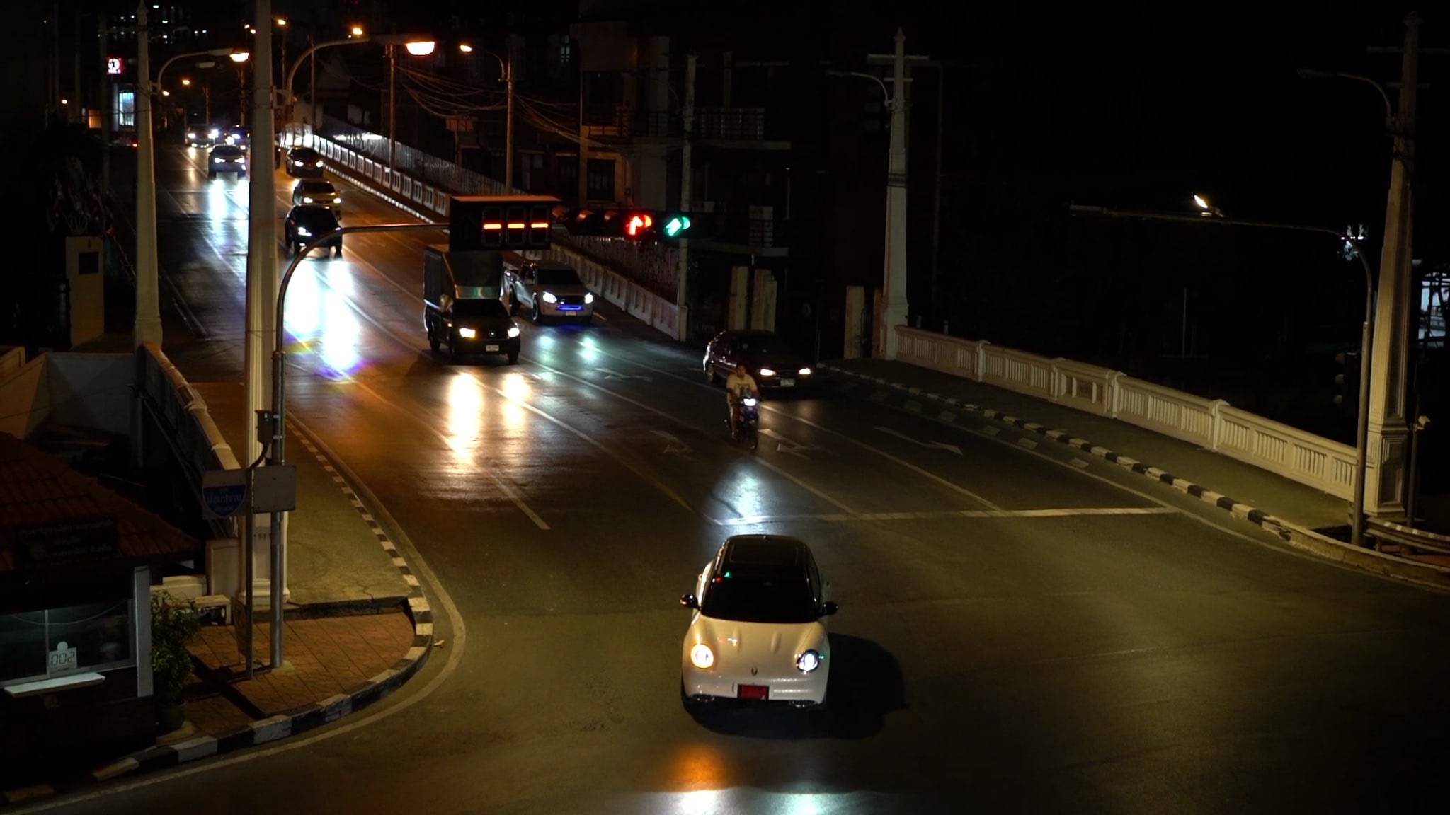 Nighttime traffic on a bridge, with a white car in the foreground.