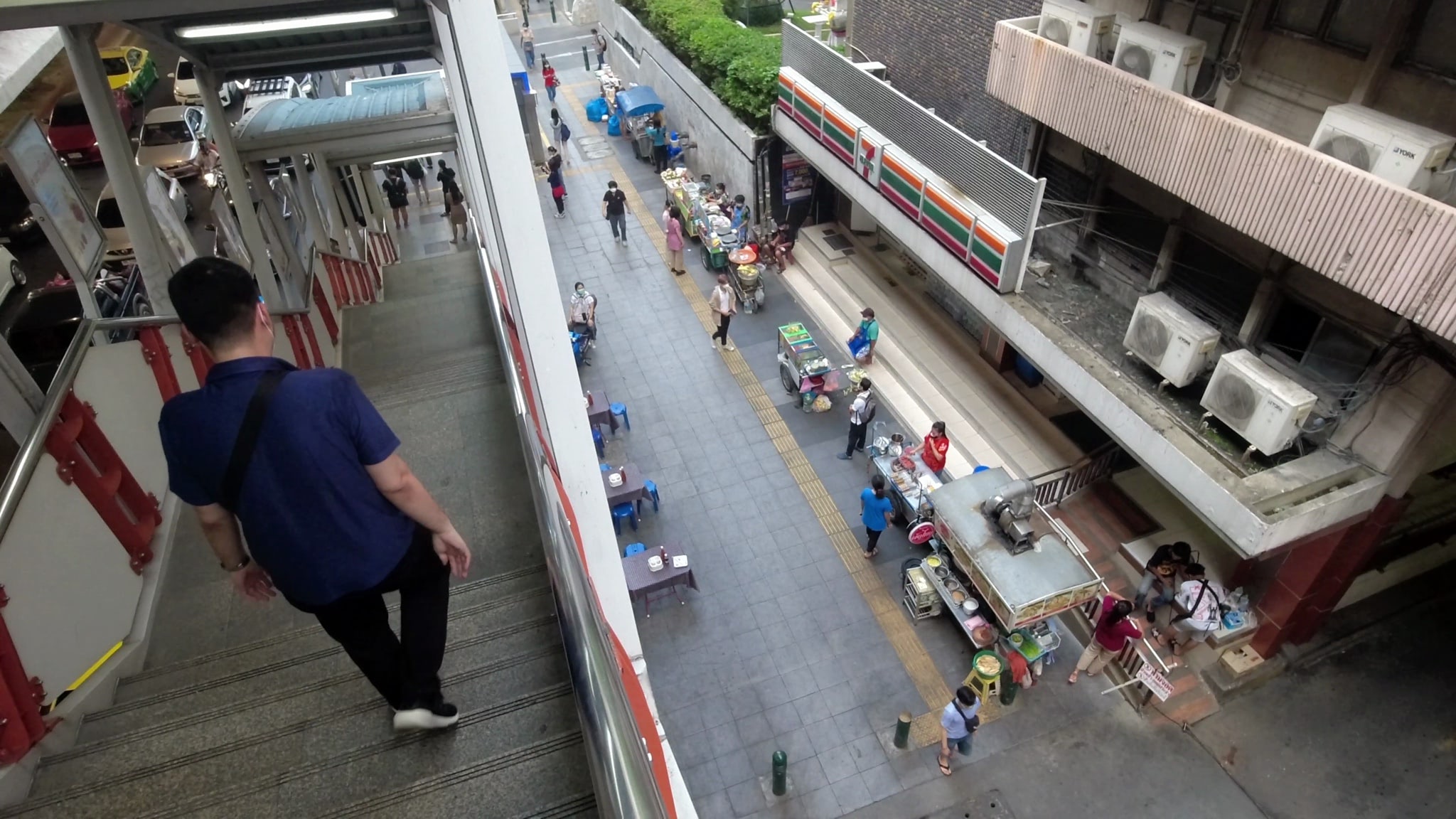 High-angle view of a Bangkok street scene with food vendors and people walking, seen from a pedestrian overpass.