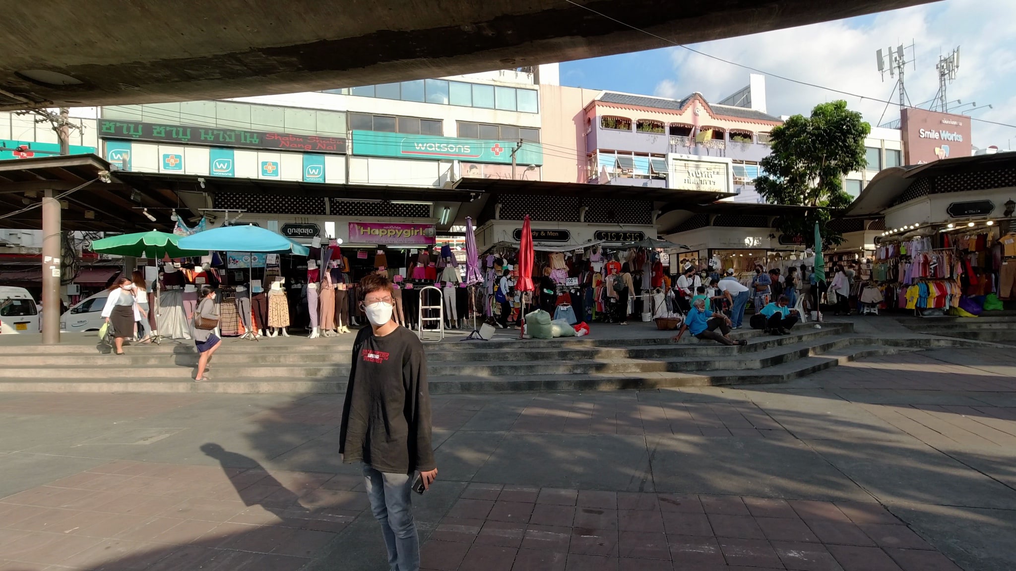 Person in mask standing in front of outdoor clothing market.