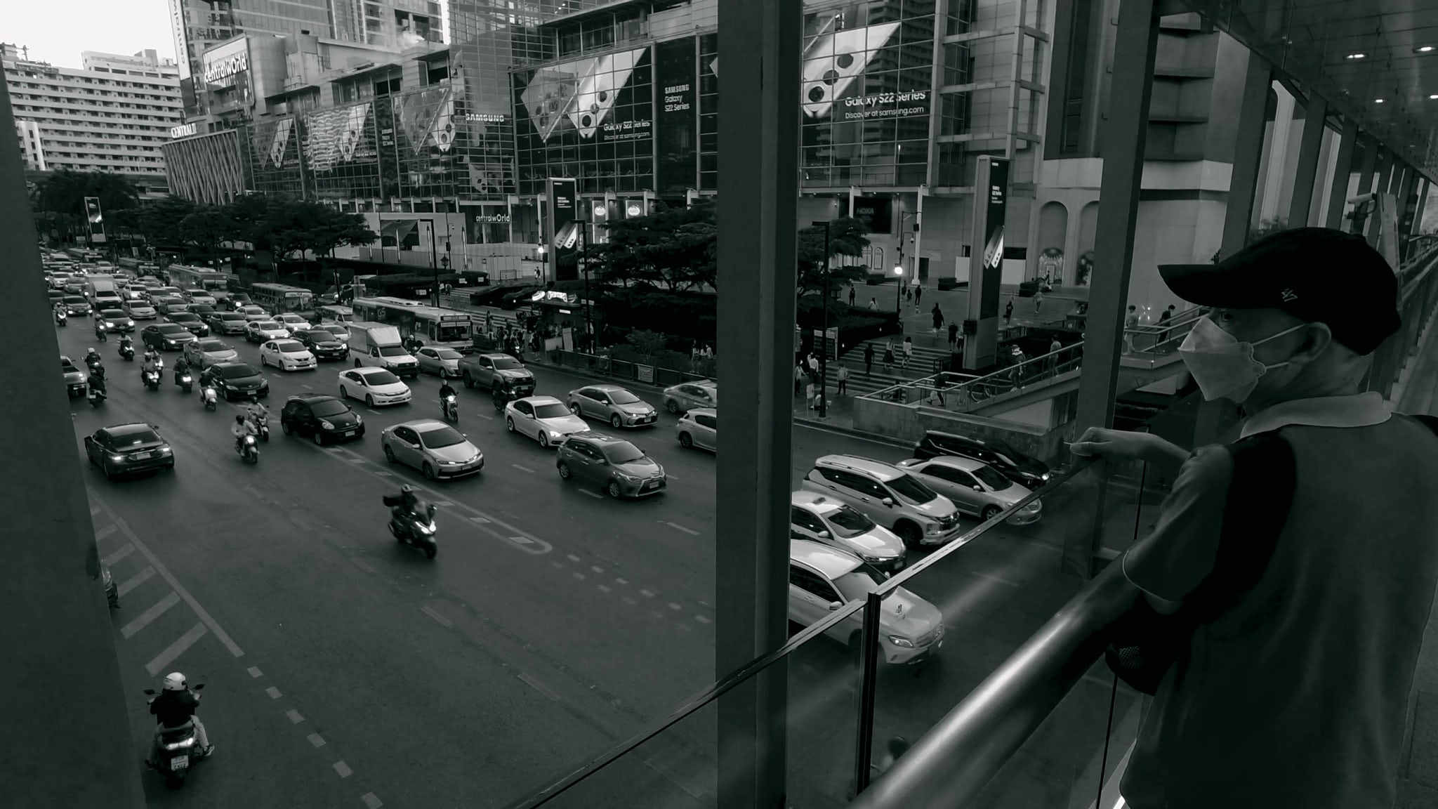 Man in face mask looking at busy city street from overpass.