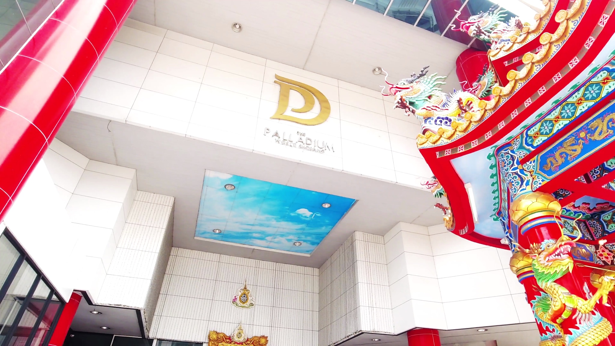 The Palladium World Shopping mall entrance in Bangkok, featuring a gold D logo and a vibrant red and gold Chinese shrine.