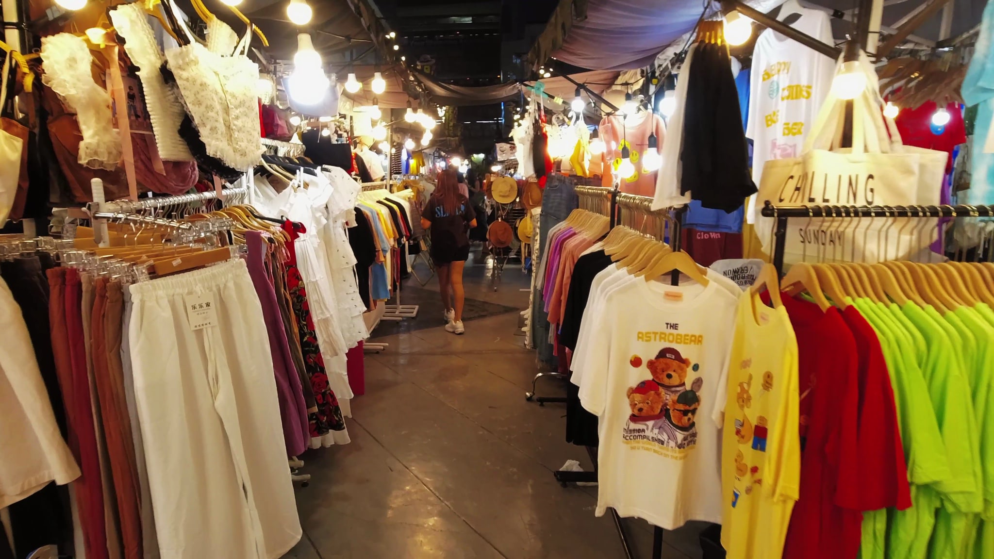 Bangkok night market clothing stalls with clothes on hangers.