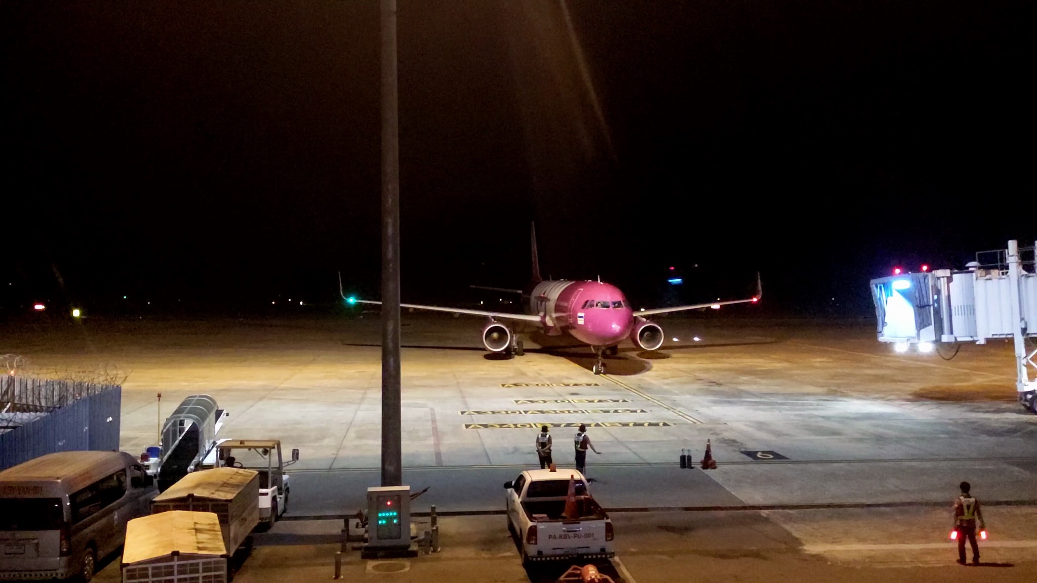 Pink airplane parked at night on the tarmac, next to a jet bridge.