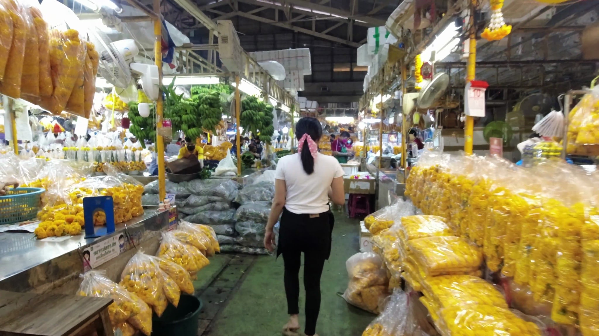 Woman walking through a Bangkok flower market filled with bags of yellow flowers.