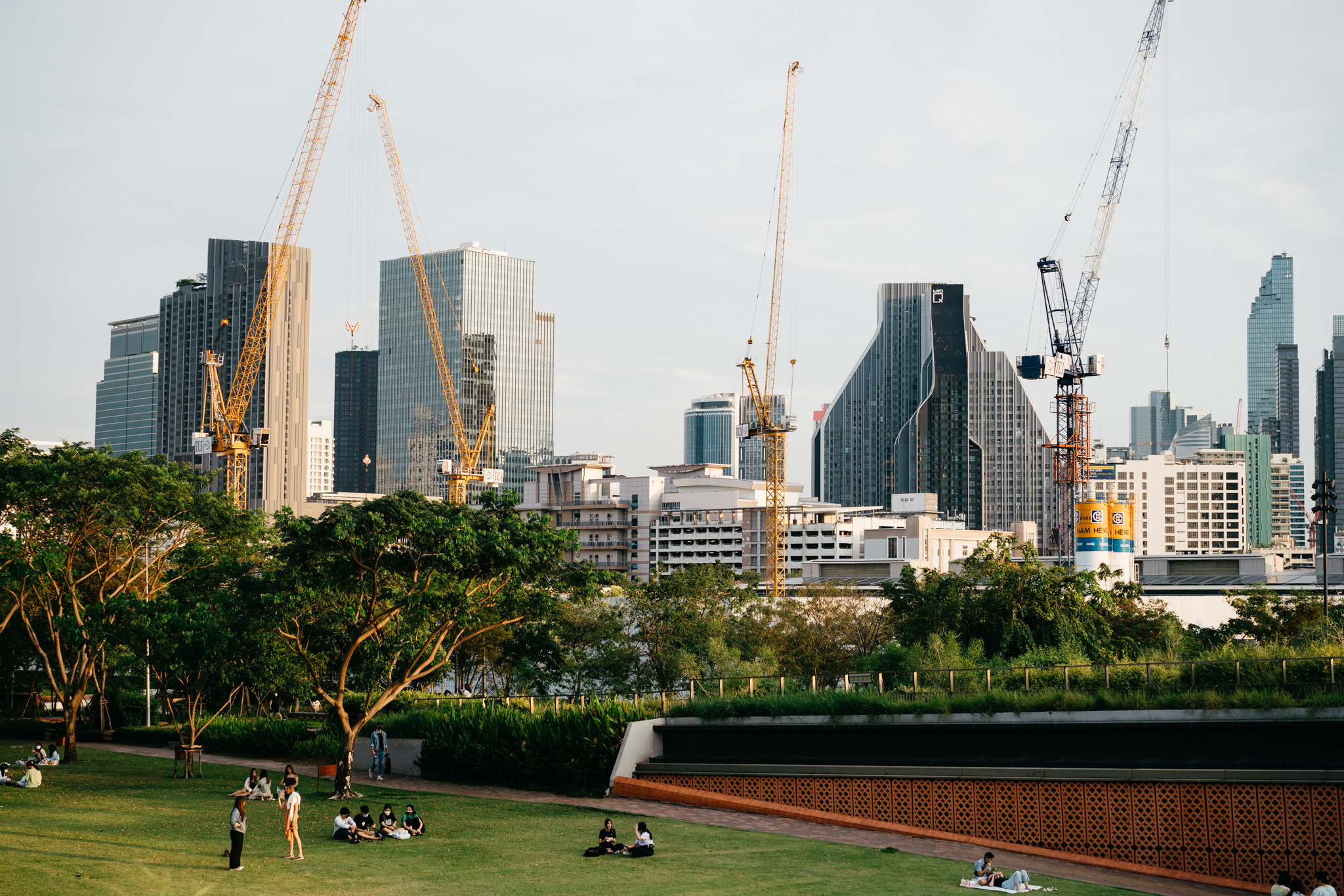 Bangkok cityscape with construction cranes and people relaxing in a park.
