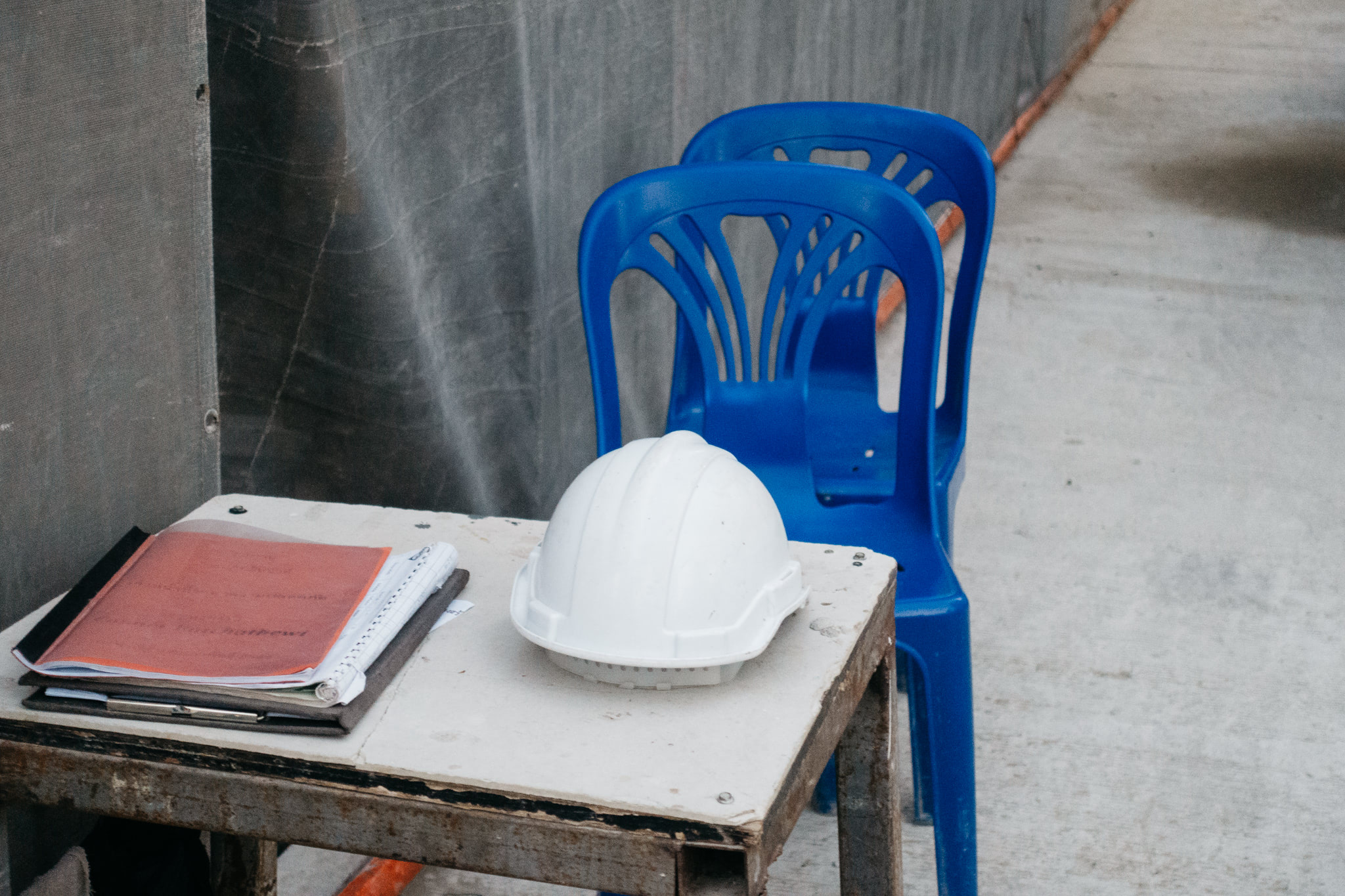 White hard hat, paperwork, and two blue plastic chairs on a small metal table.