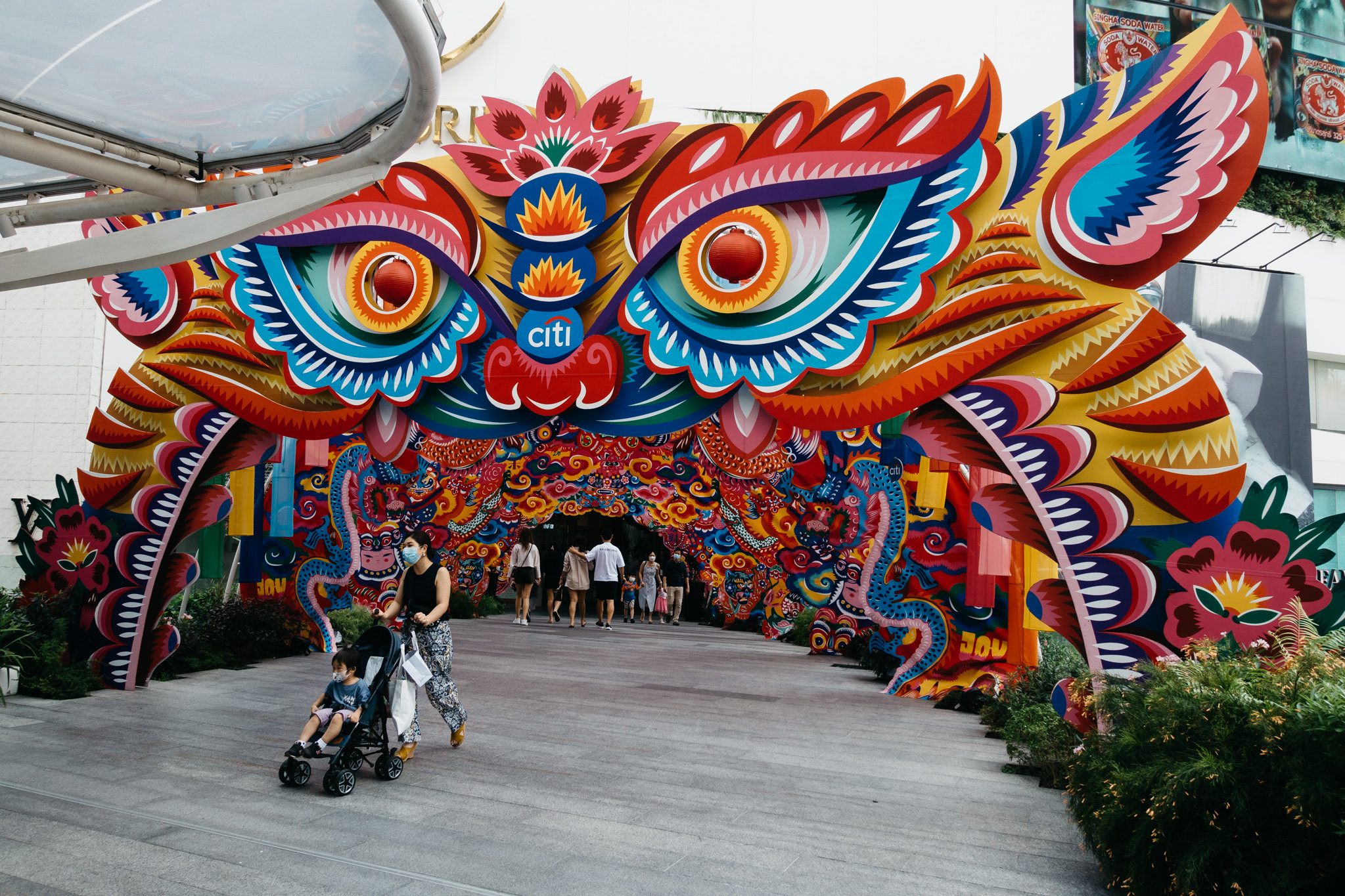 Colorful, large-scale artwork forming an archway entrance; a woman with a stroller and child walk through.