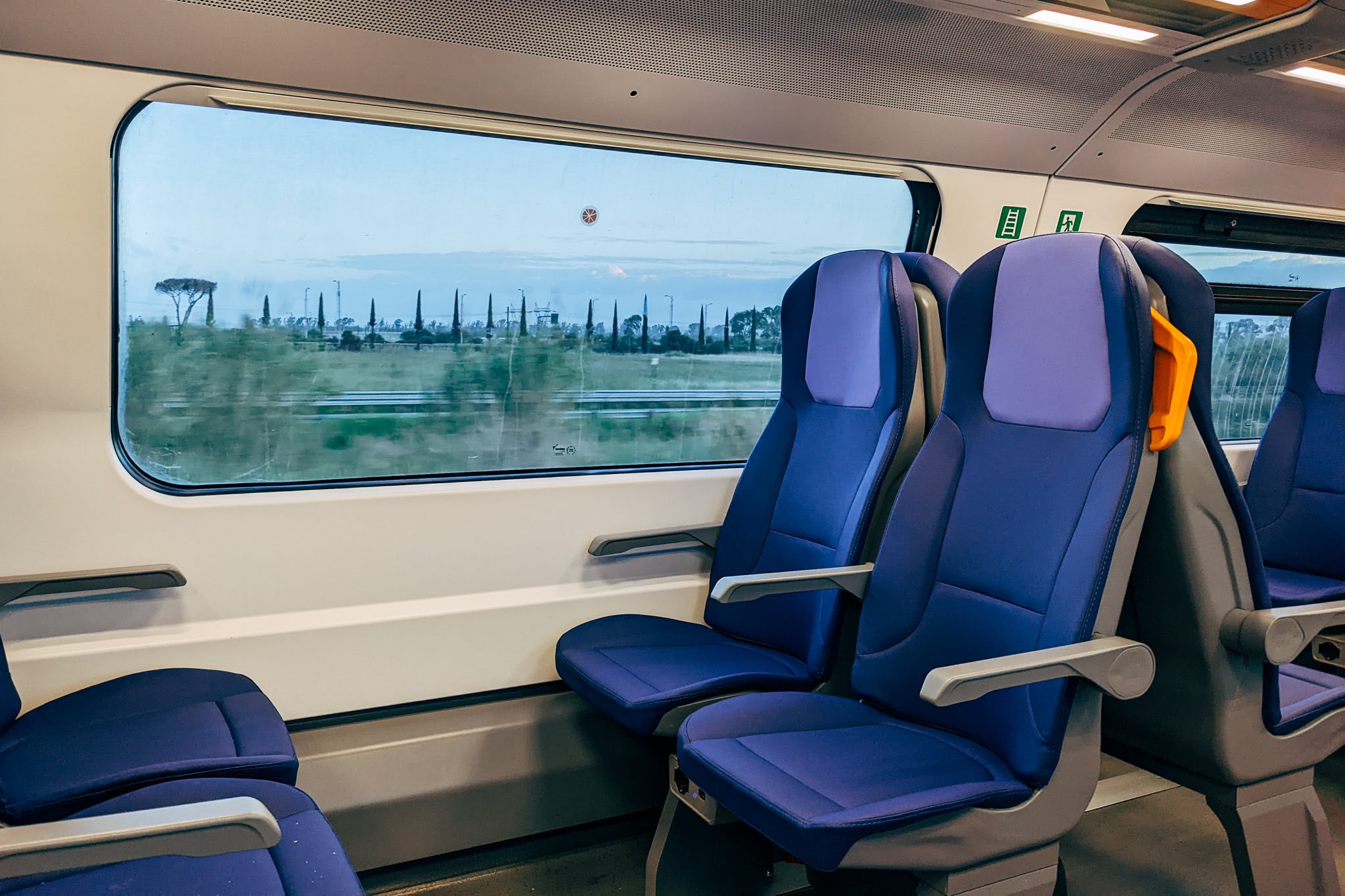 Empty blue train seats next to a window showing a blurry Italian landscape.