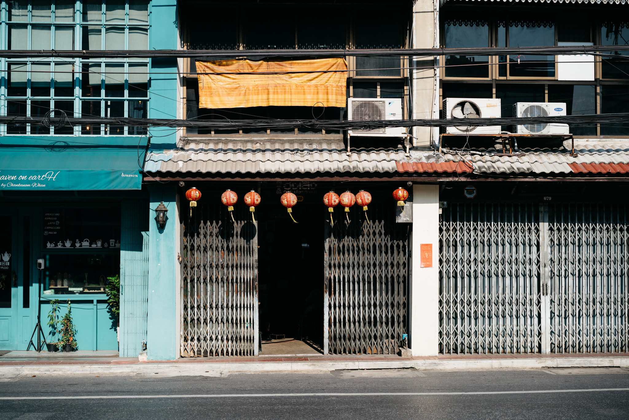 Red lanterns hang above a closed metal storefront gate in Bangkok, China.