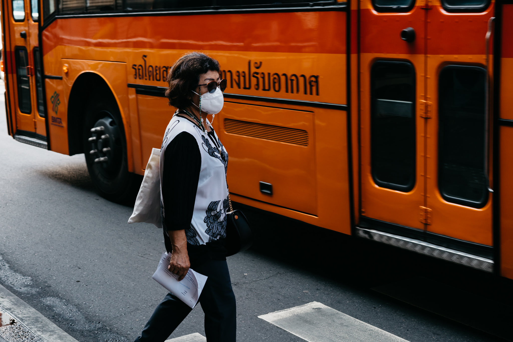 Woman wearing a mask walking past an orange bus.
