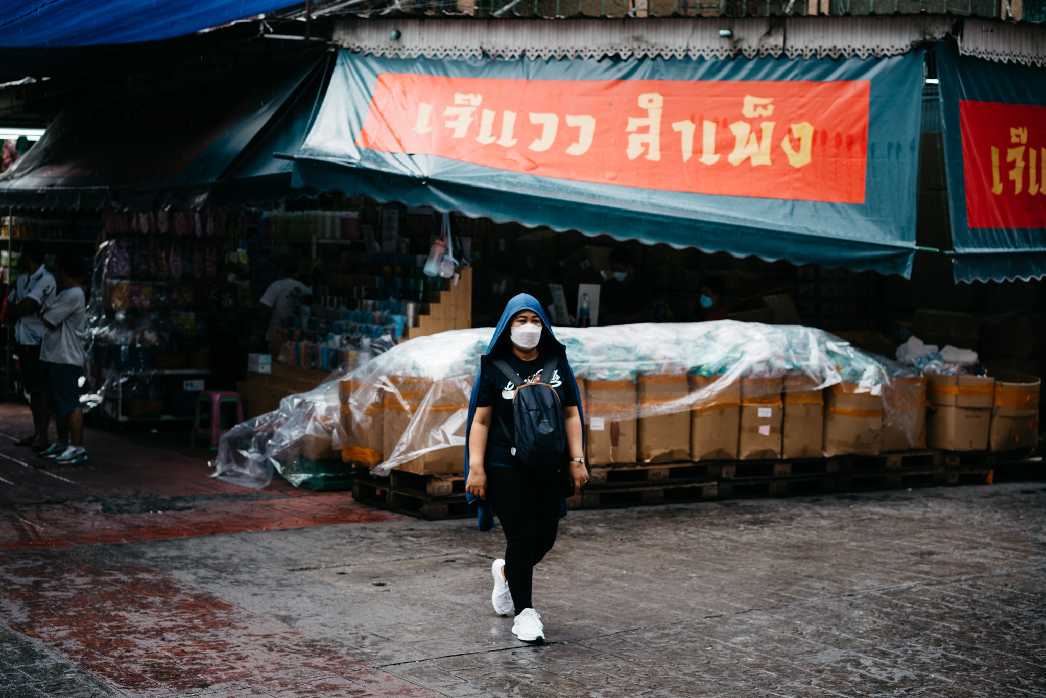 Person wearing a face mask and hooded jacket walking in Bangkok's Chinatown during the rain.