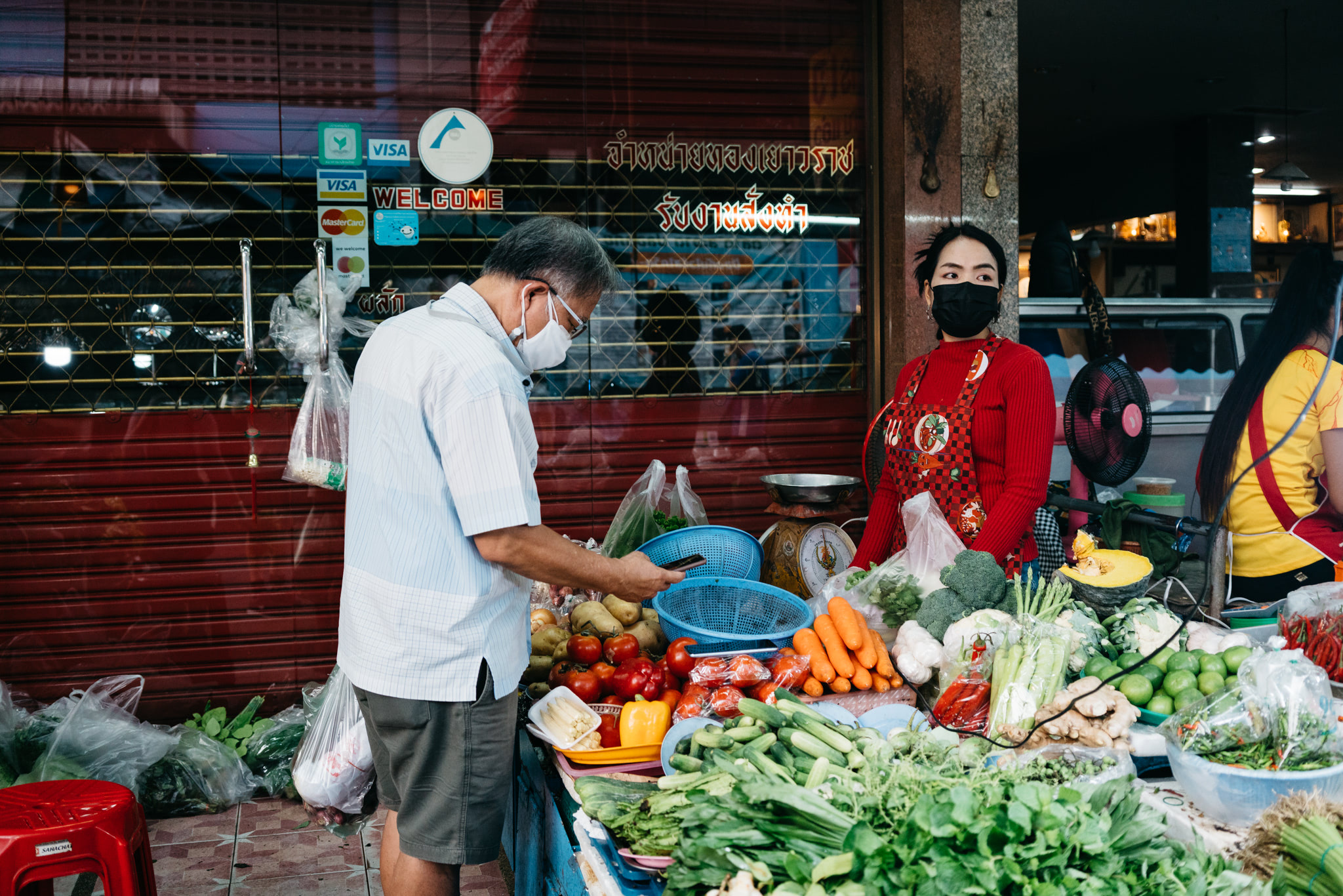 Bangkok market vendor selling produce to a masked customer.