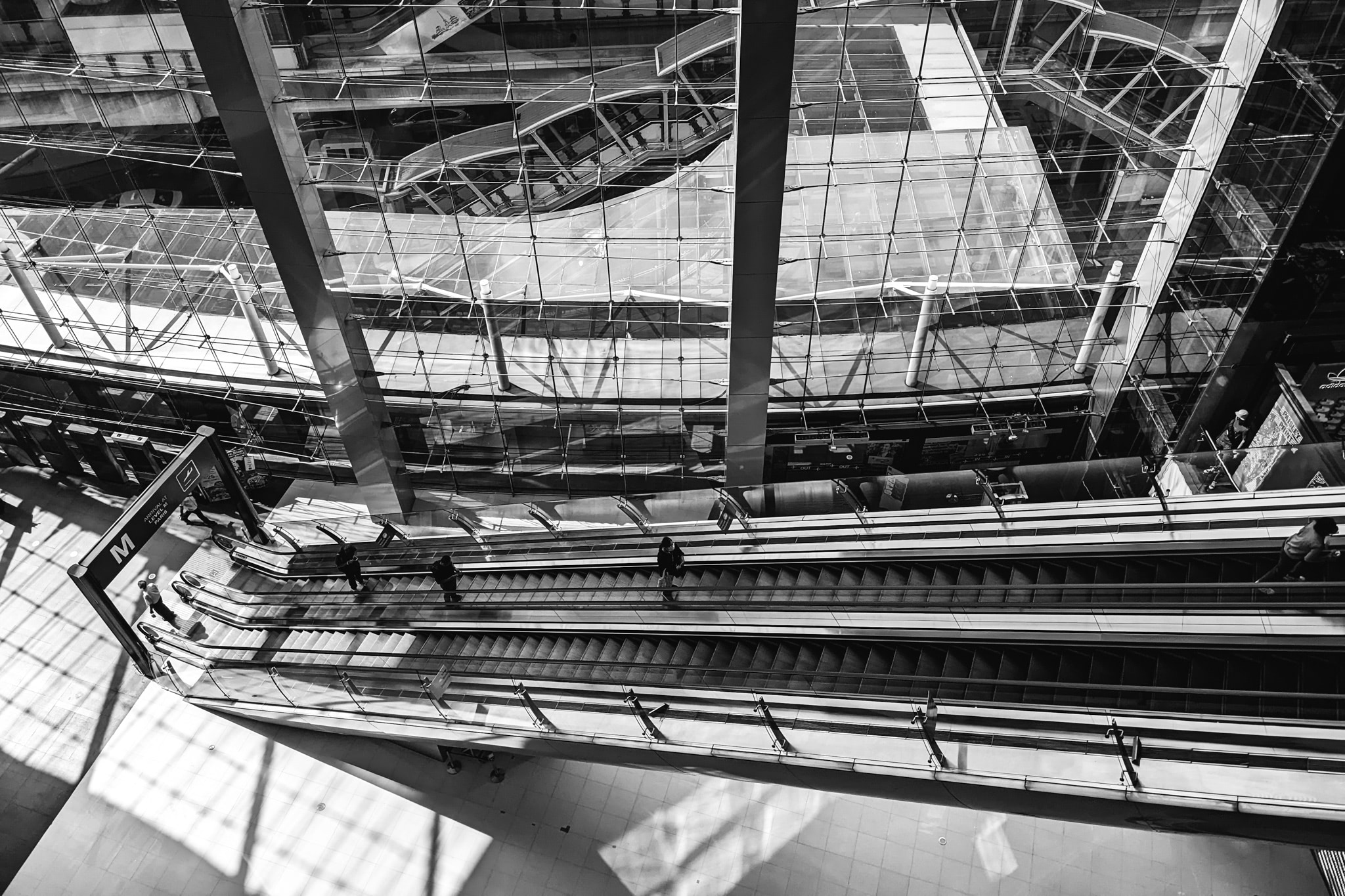 High-angle black and white photo of escalators in a modern Bangkok shopping mall.