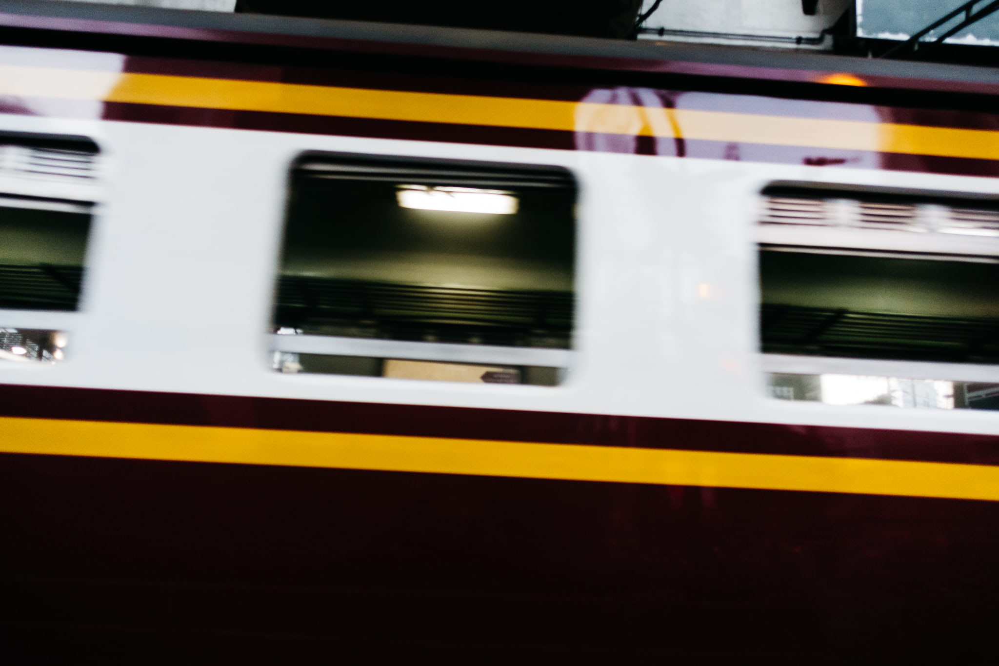 Blurred image of a maroon and gold train car in motion.