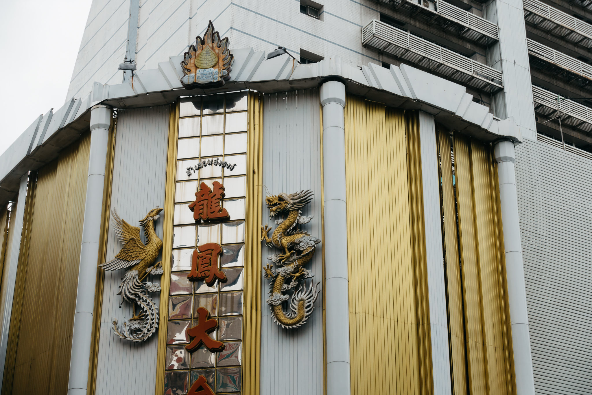 Close-up of a building facade with gold and white panels, featuring golden dragon and phoenix sculptures and Chinese characters.