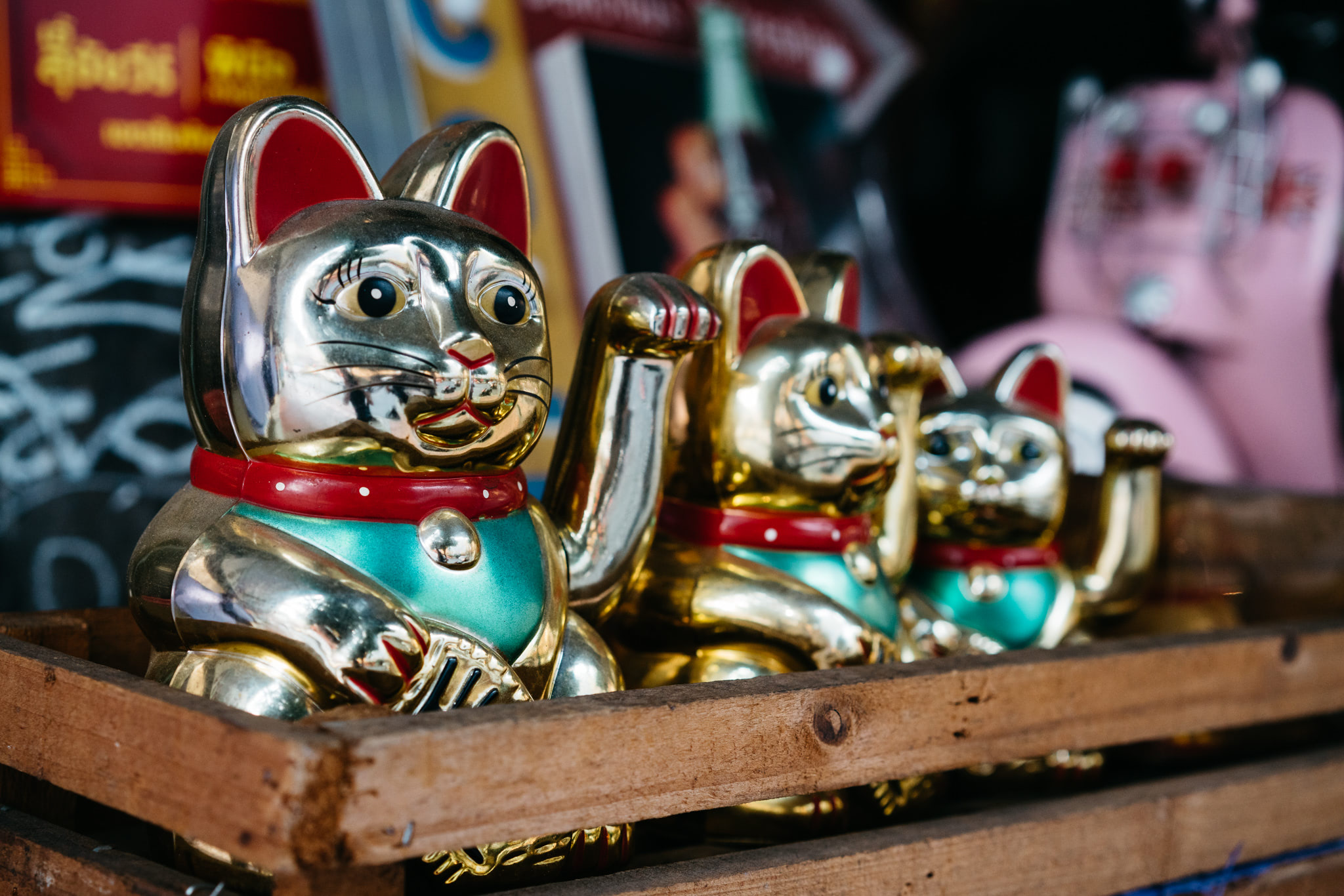 Three gold Maneki-neko (beckoning cat) figurines in a wooden crate.