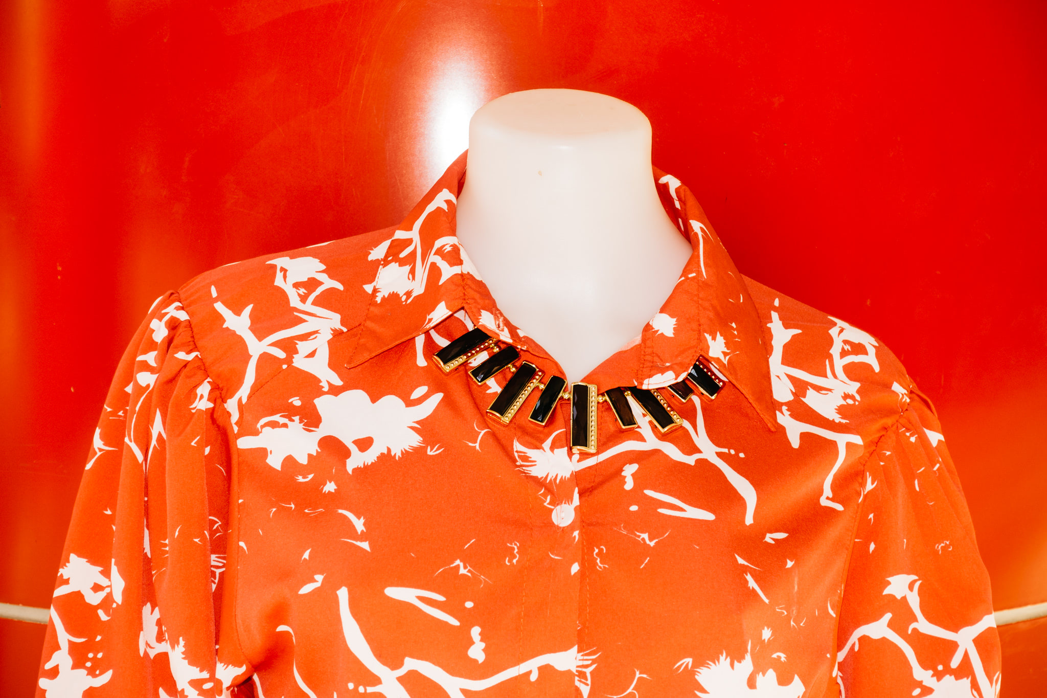 Orange shirt with white abstract print and gold and black necklace on mannequin.